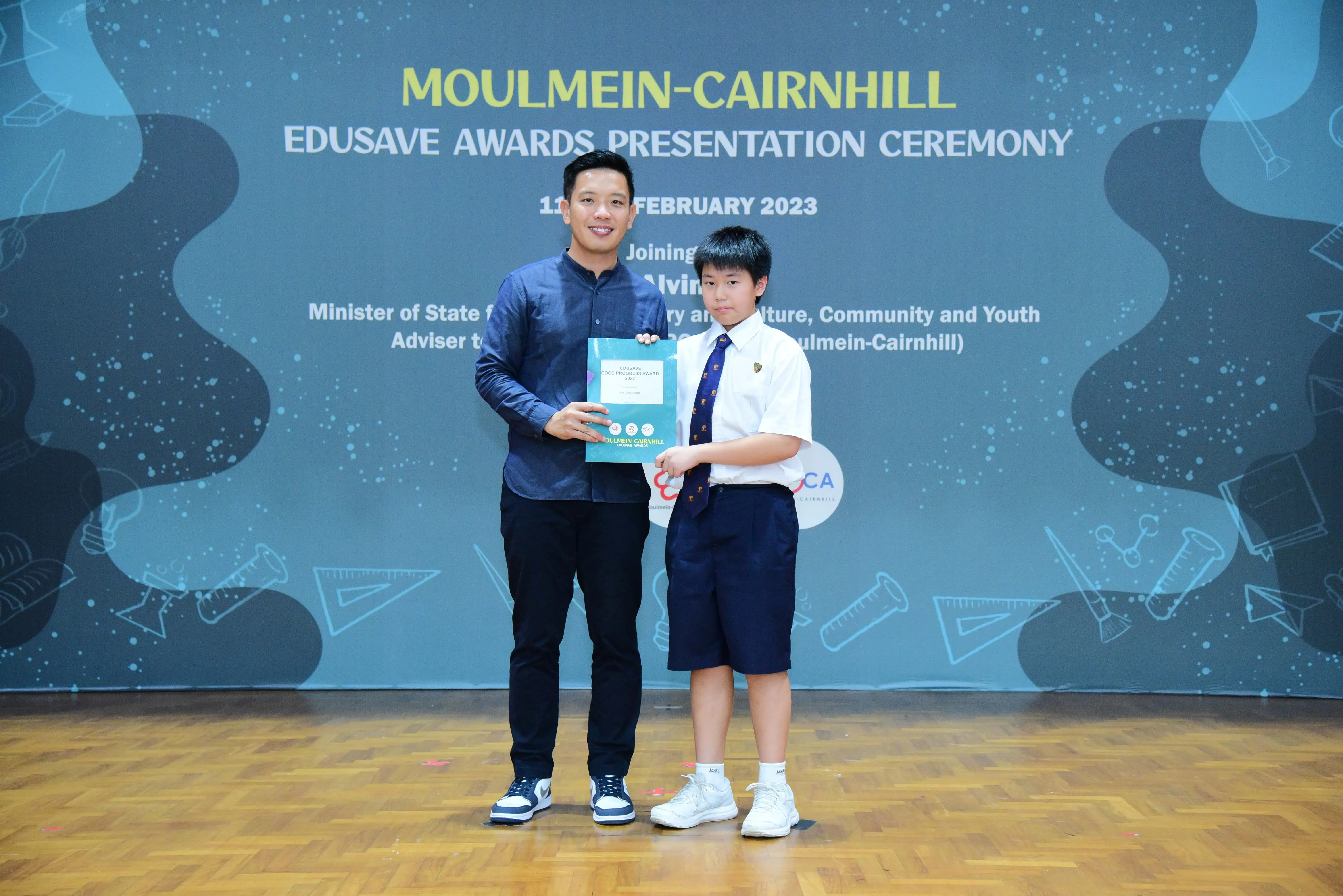 An adult and a uniformed student hold an award together at the Moulmein-Cairnhill Edusave Awards Ceremony, February 2023.