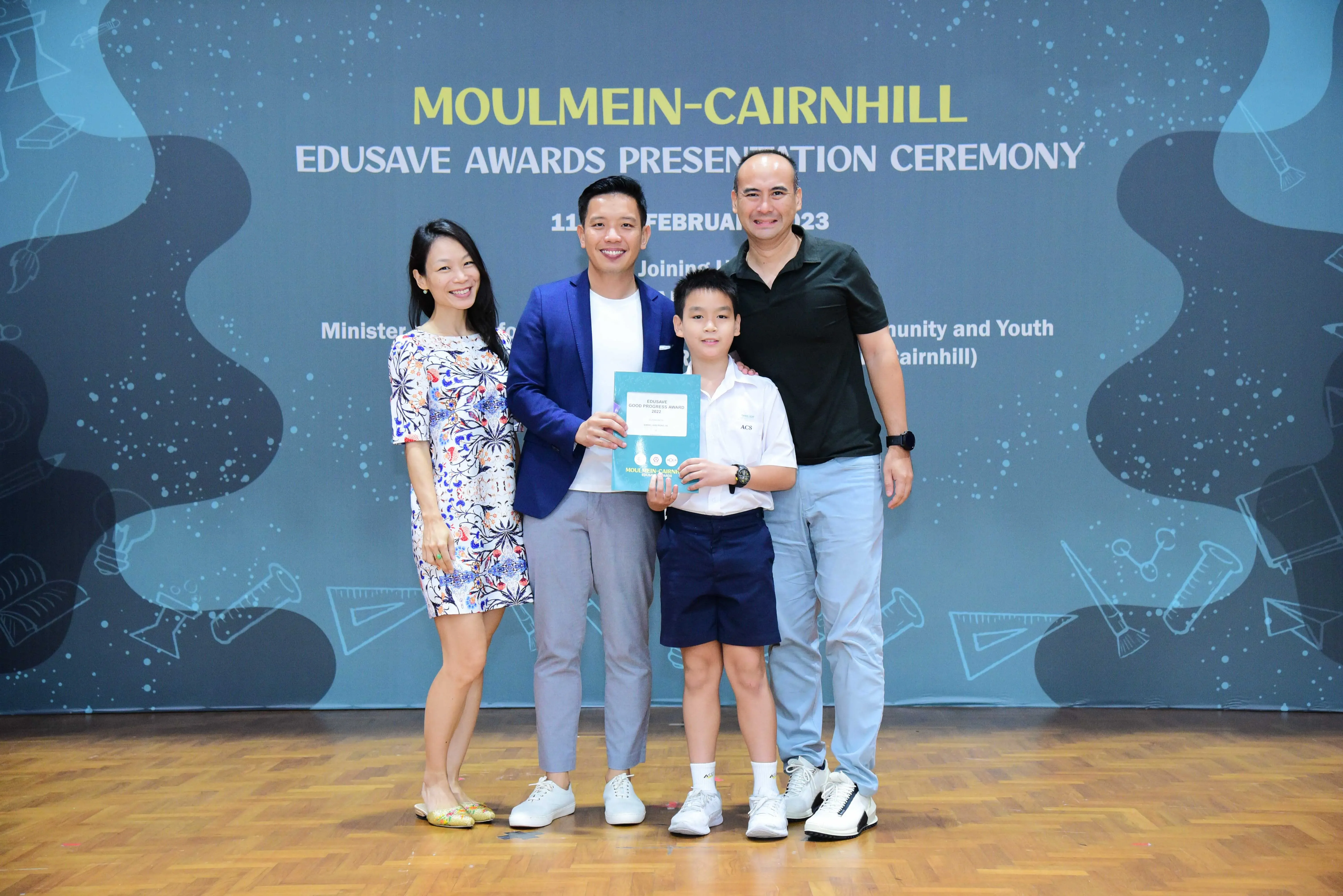 Four people pose at the Moulmein-Cairnhill Edusave Awards Presentation Ceremony, with a boy holding a certificate.