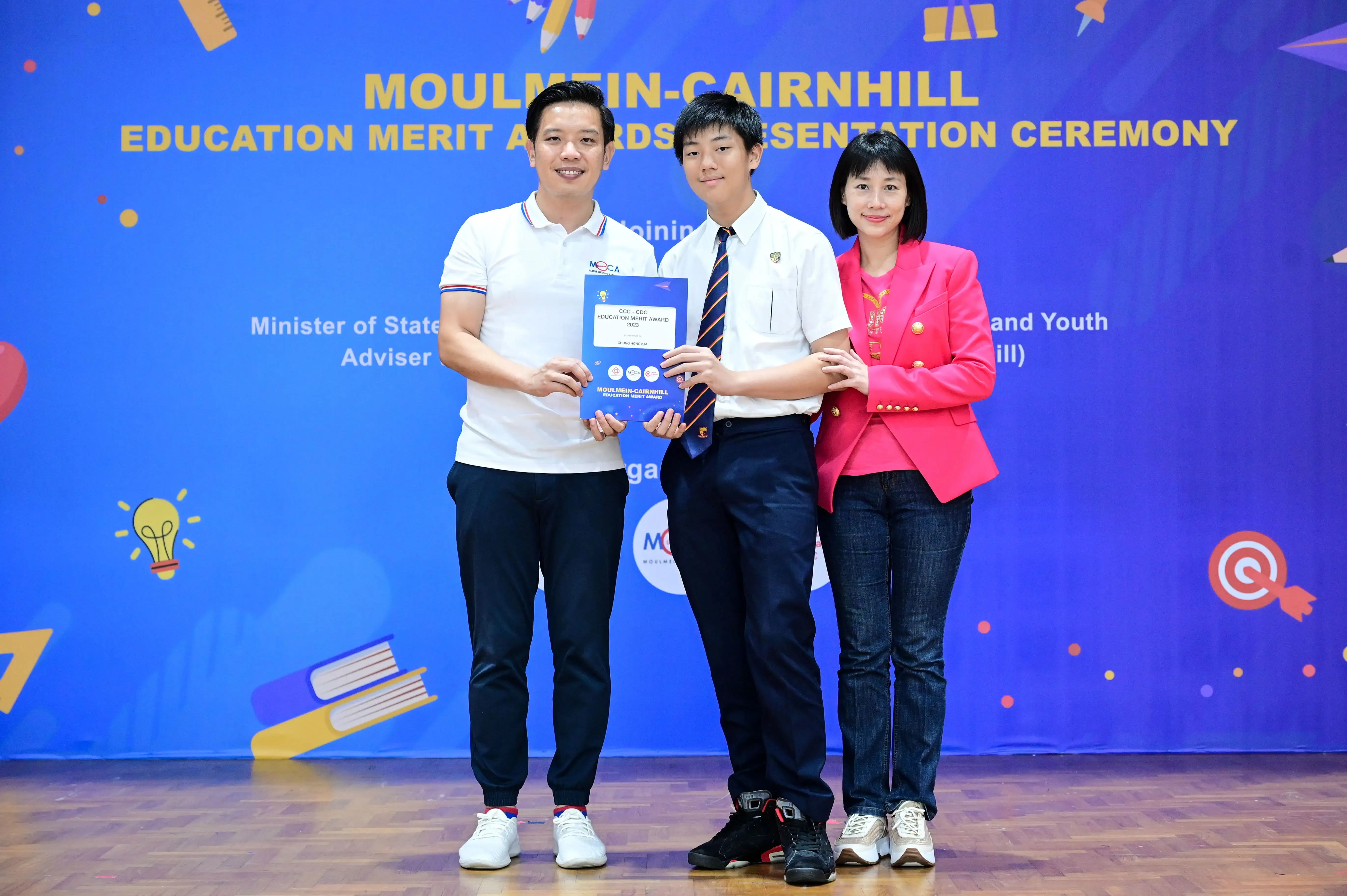 Three people pose at the Moulmein-Cairnhill Education Merit Awards Presentation Ceremony, with a student holding an award.