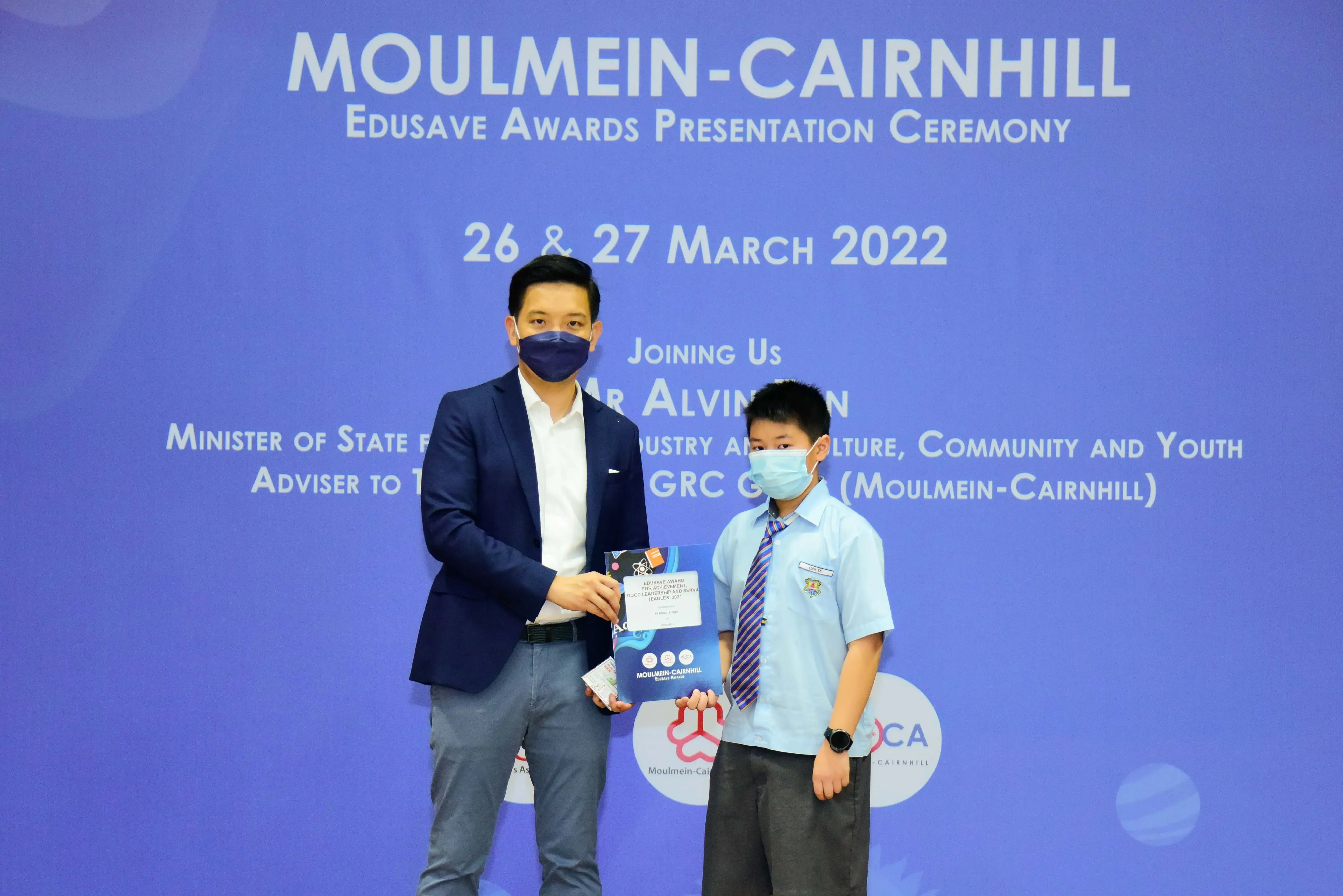 Two masked individuals hold an award at the Moulmein-Cairnhill Edusave Awards Presentation Ceremony, March 2022.