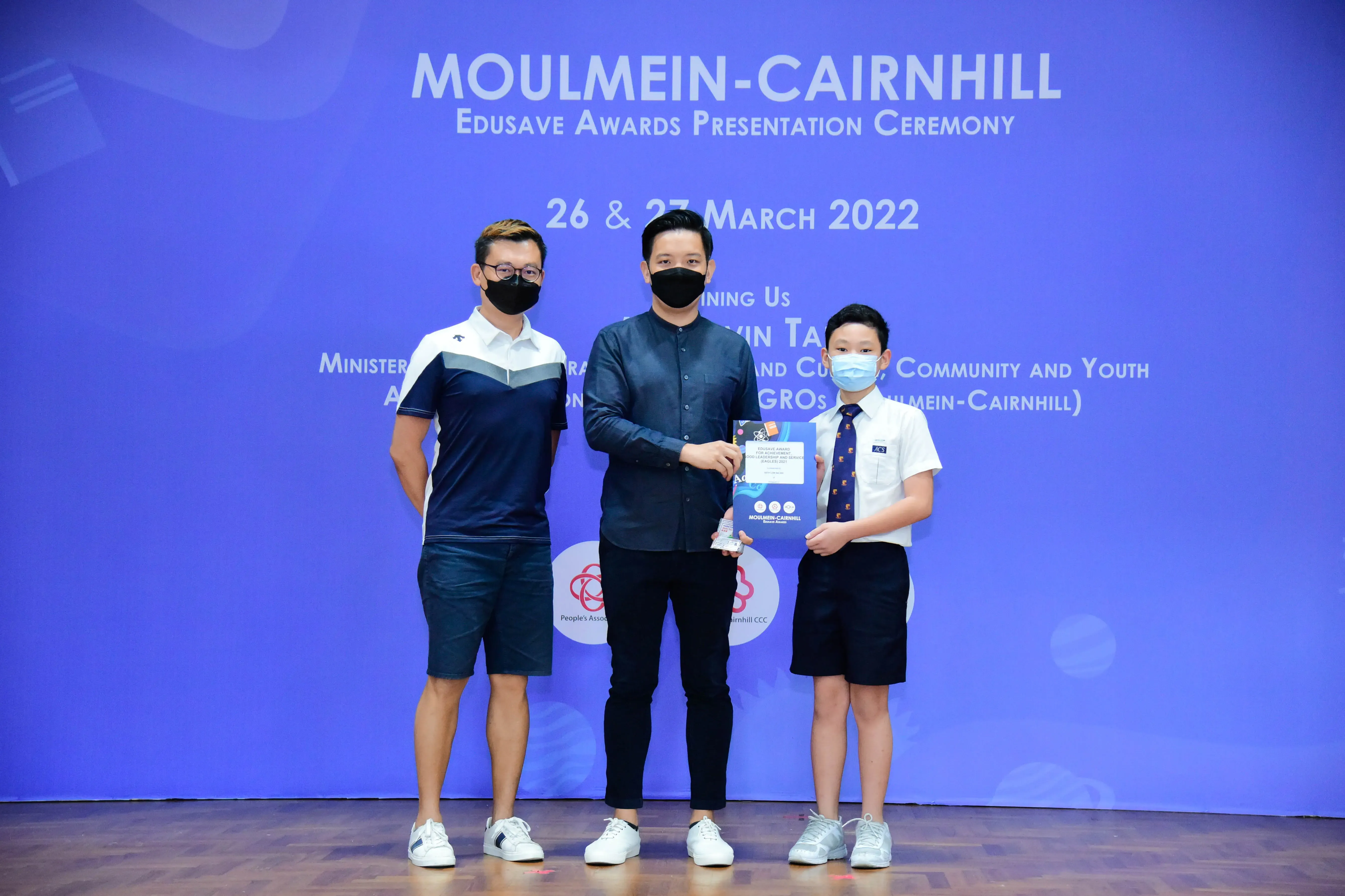 Two masked men and a masked boy in school uniform pose at the Moulmein-Cairnhill Edusave Awards Ceremony, March 2022.