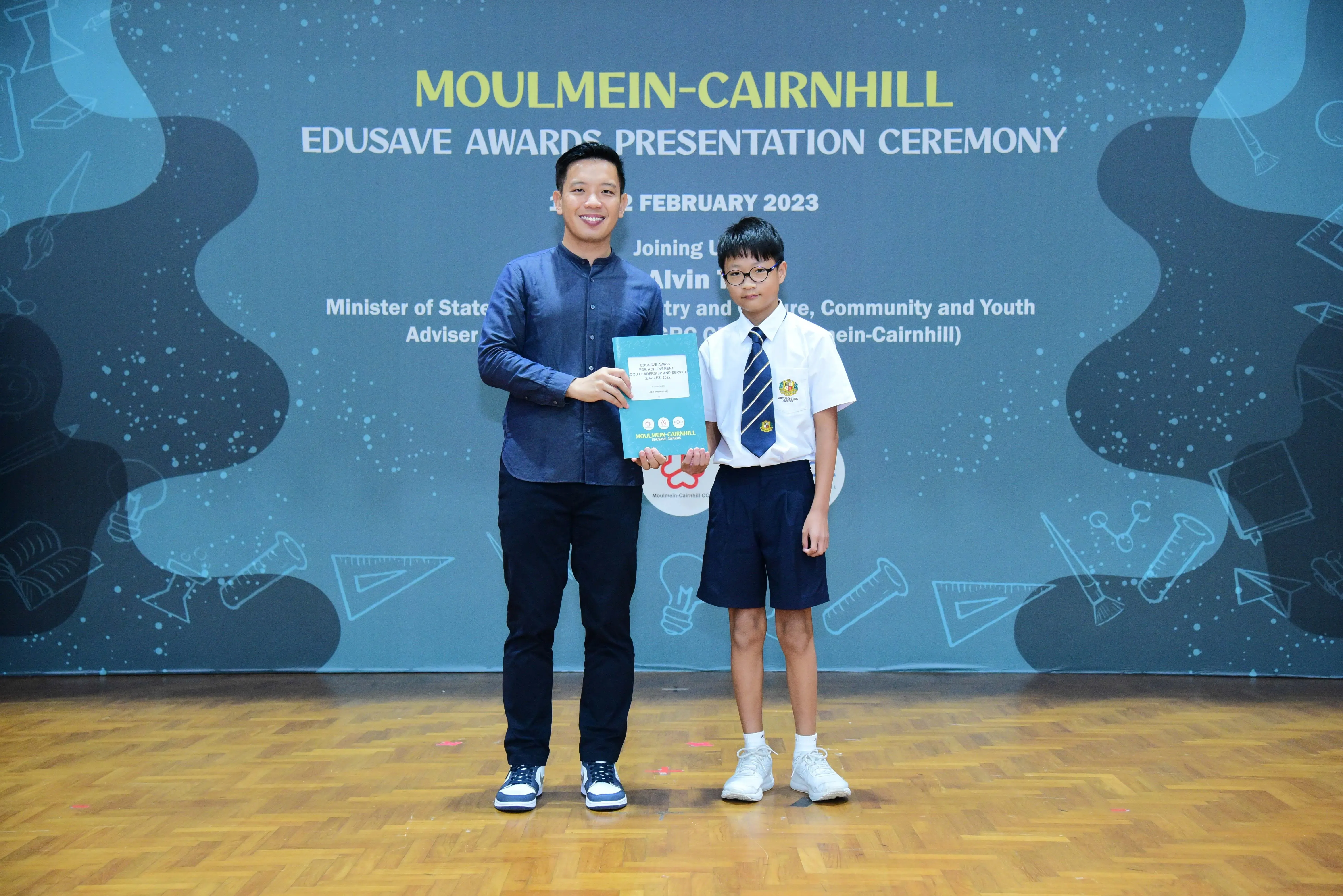 An adult and a uniformed schoolboy hold an award booklet at the Moulmein-Cairnhill Edusave Awards Ceremony, February 2023.