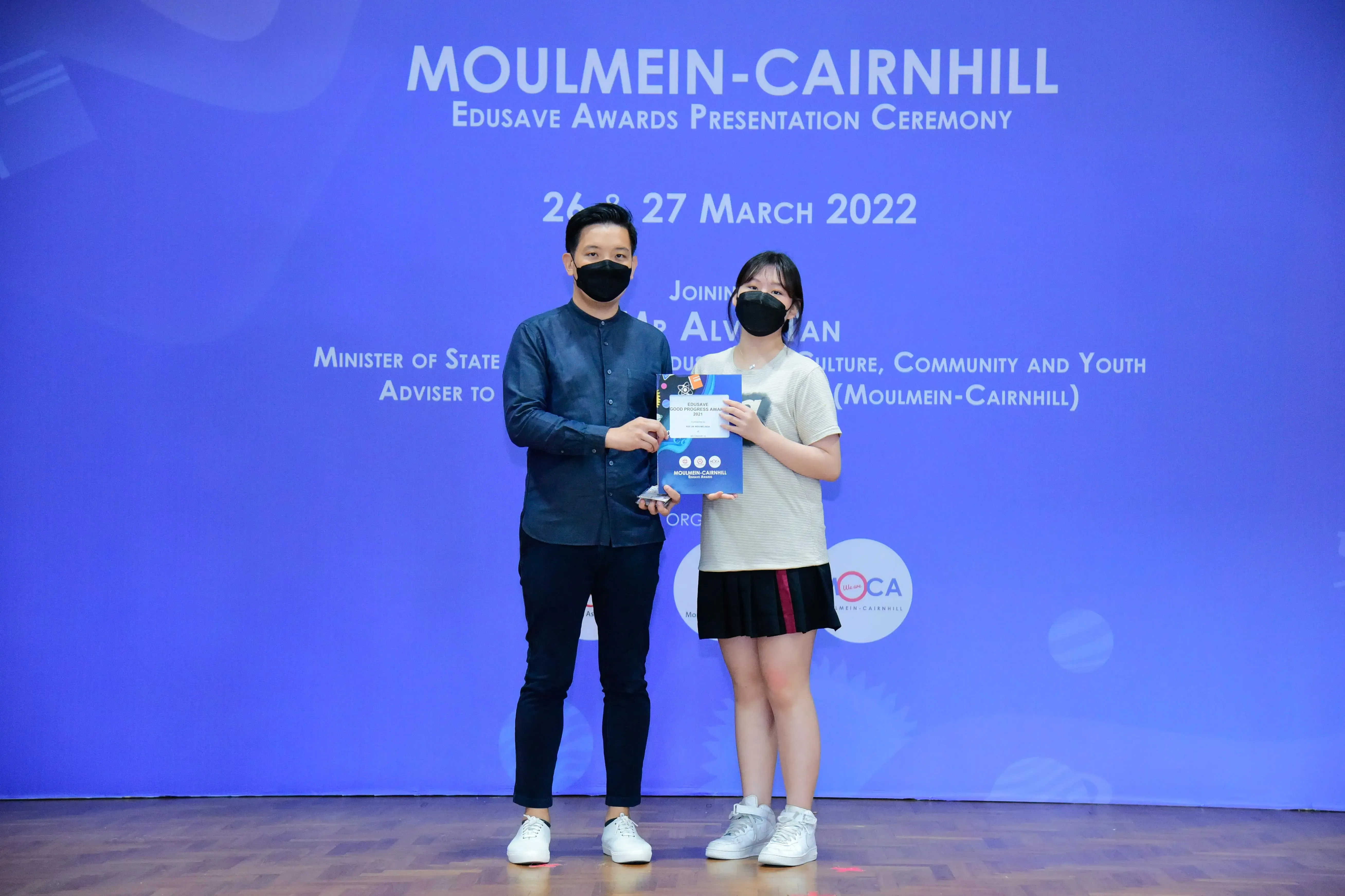 Two masked people hold an award certificate at the Moulmein-Cairnhill Edusave Awards Ceremony, March 2022.