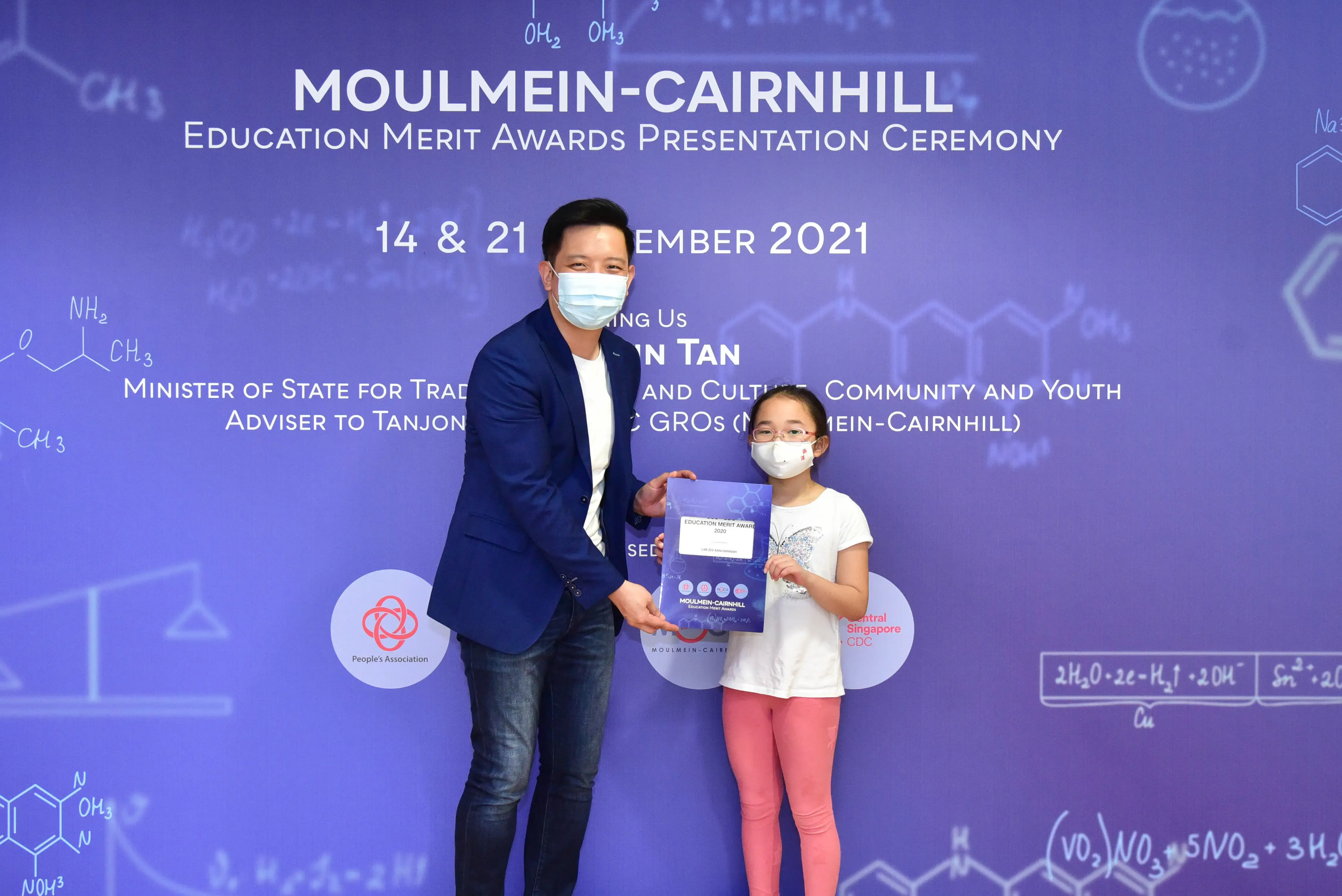 A man and young girl wearing masks hold an award certificate at the Moulmein-Cairnhill Education Merit Awards 2021.