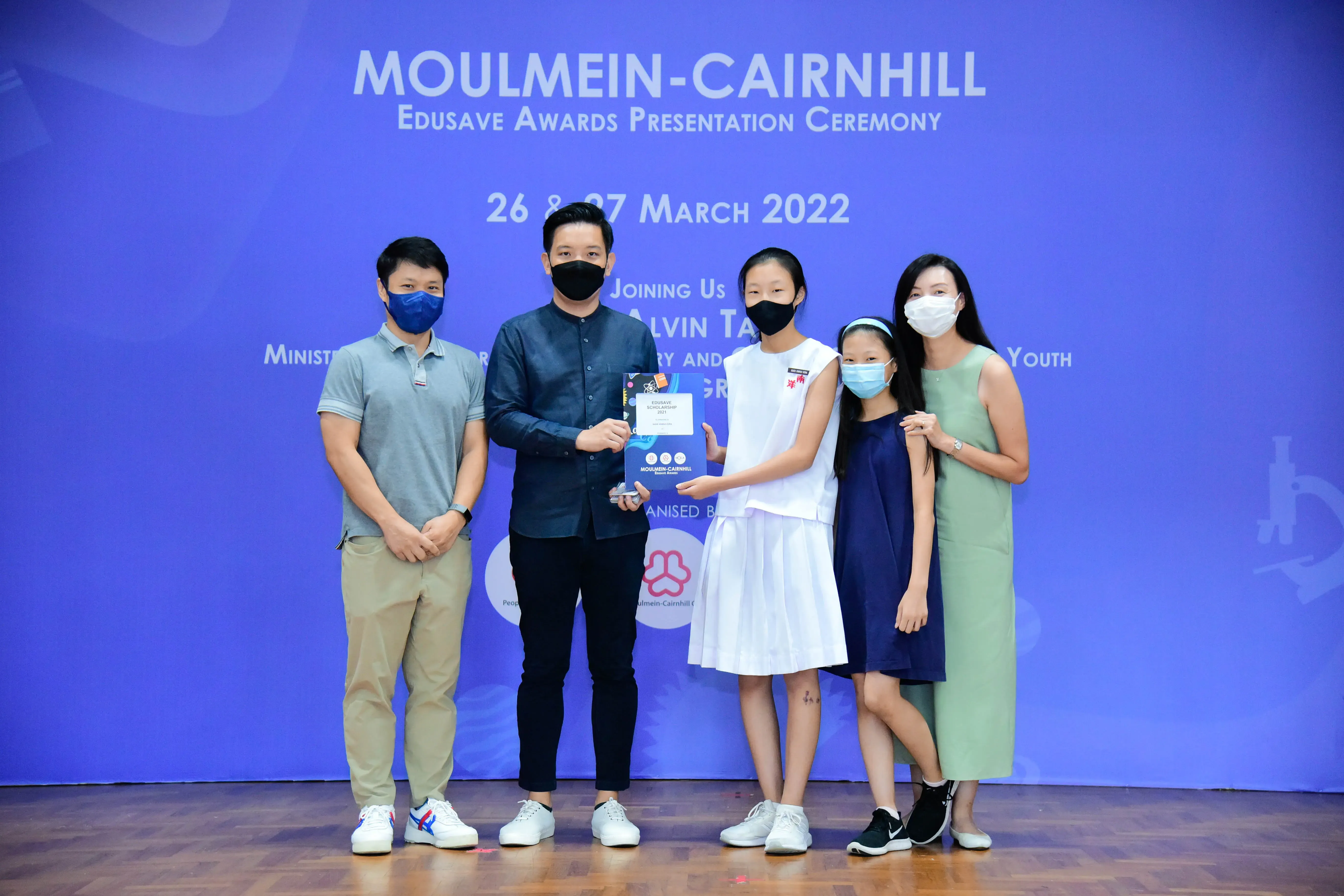 Five masked people pose on stage at the Moulmein-Cairnhill Edusave Awards Presentation Ceremony, March 2022.