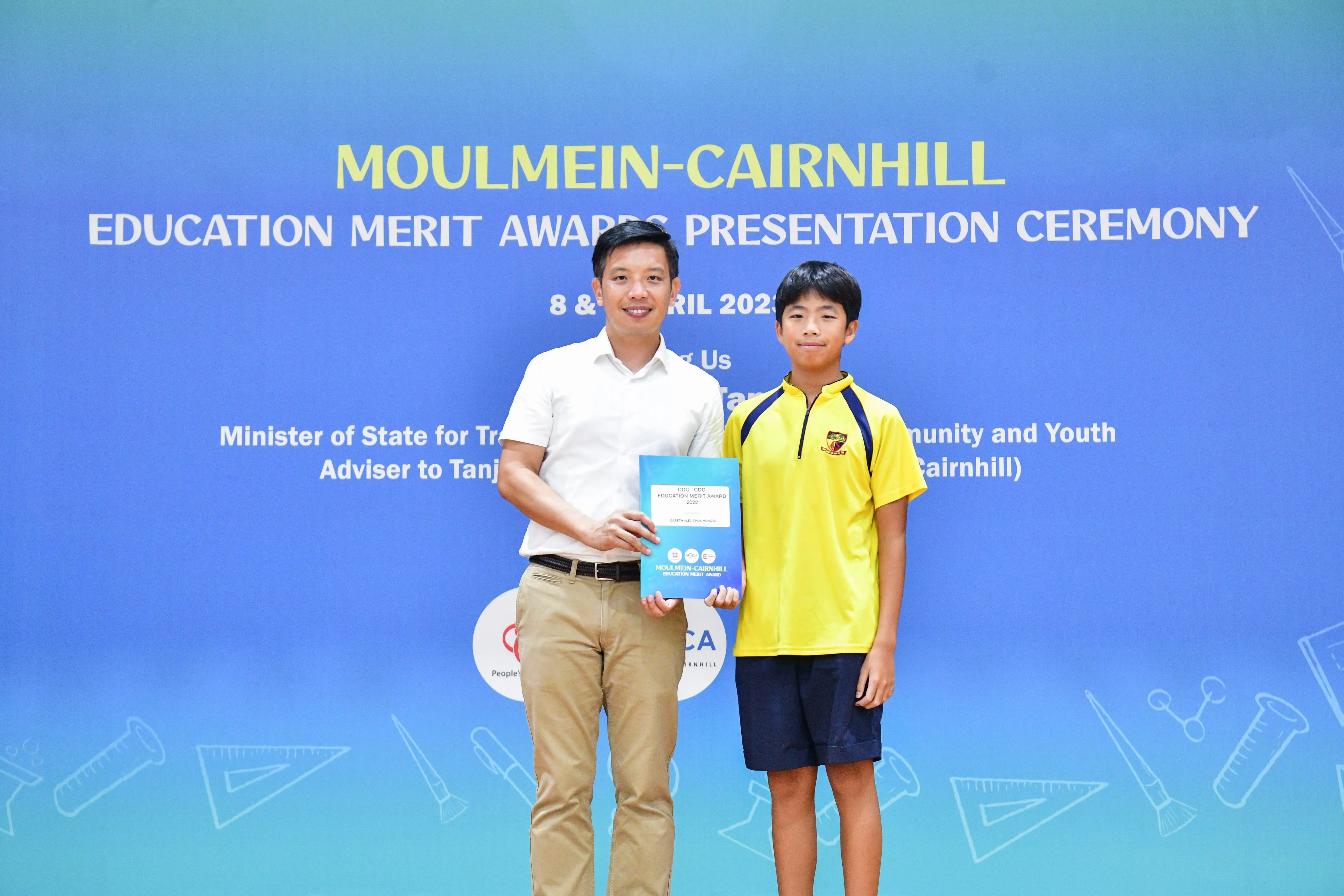 An adult man and a young boy hold an award certificate at the Moulmein-Cairnhill Education Merit Awards Ceremony.
