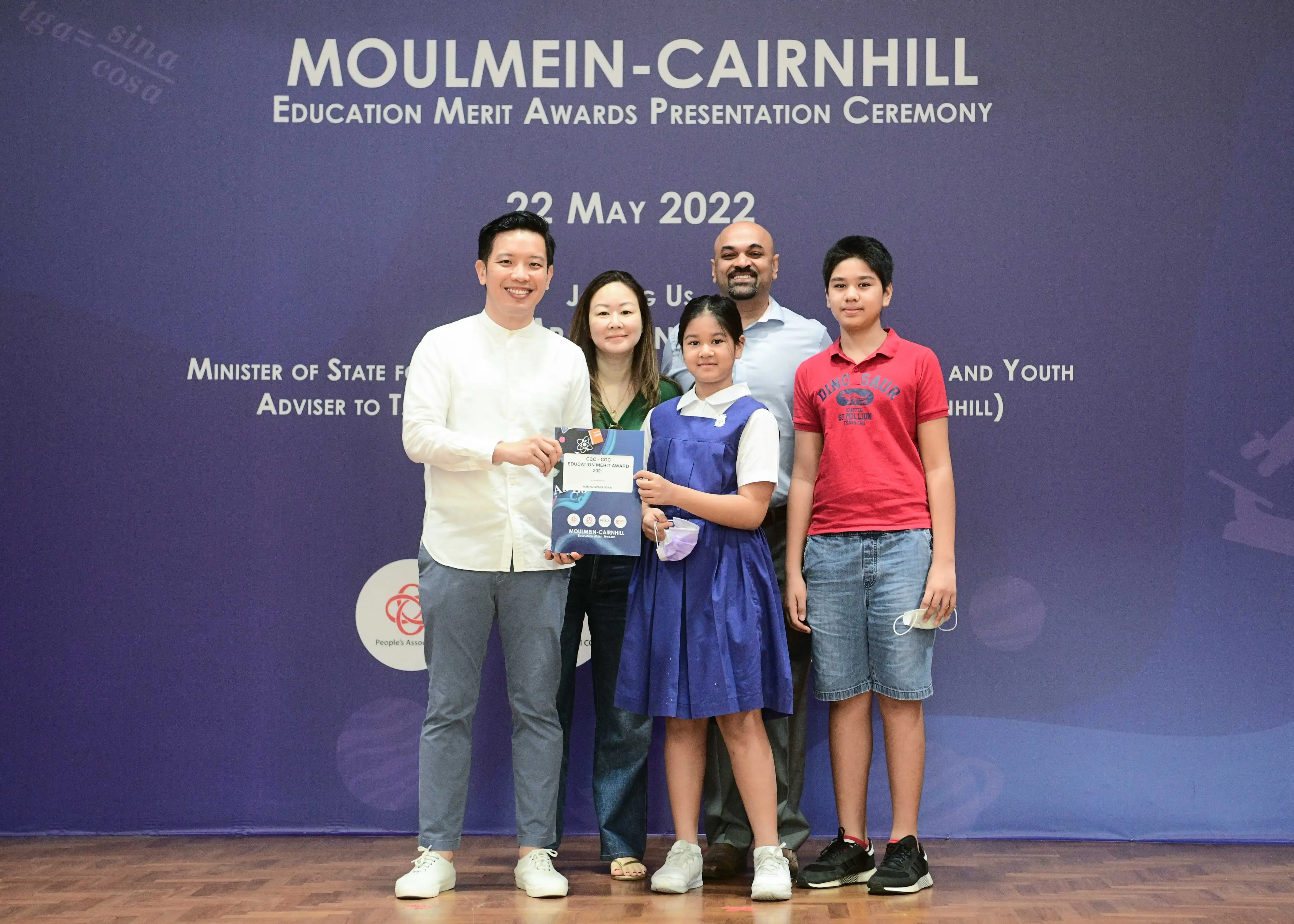 Five people pose in front of a Moulmein-Cairnhill Education Merit Awards banner dated 22 May 2022.