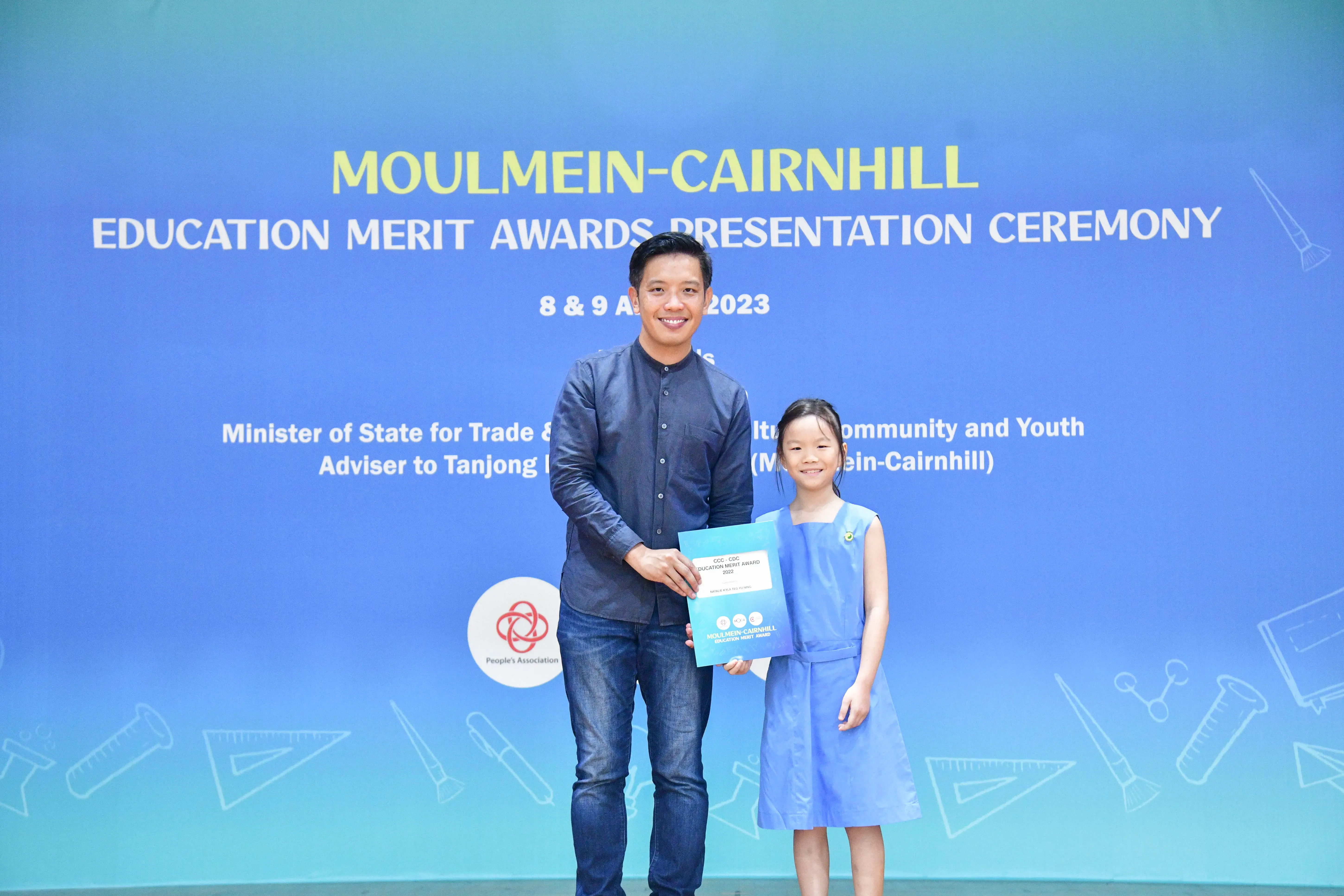 Man and young girl hold an award certificate at the Moulmein-Cairnhill Education Merit Awards Ceremony 2023.