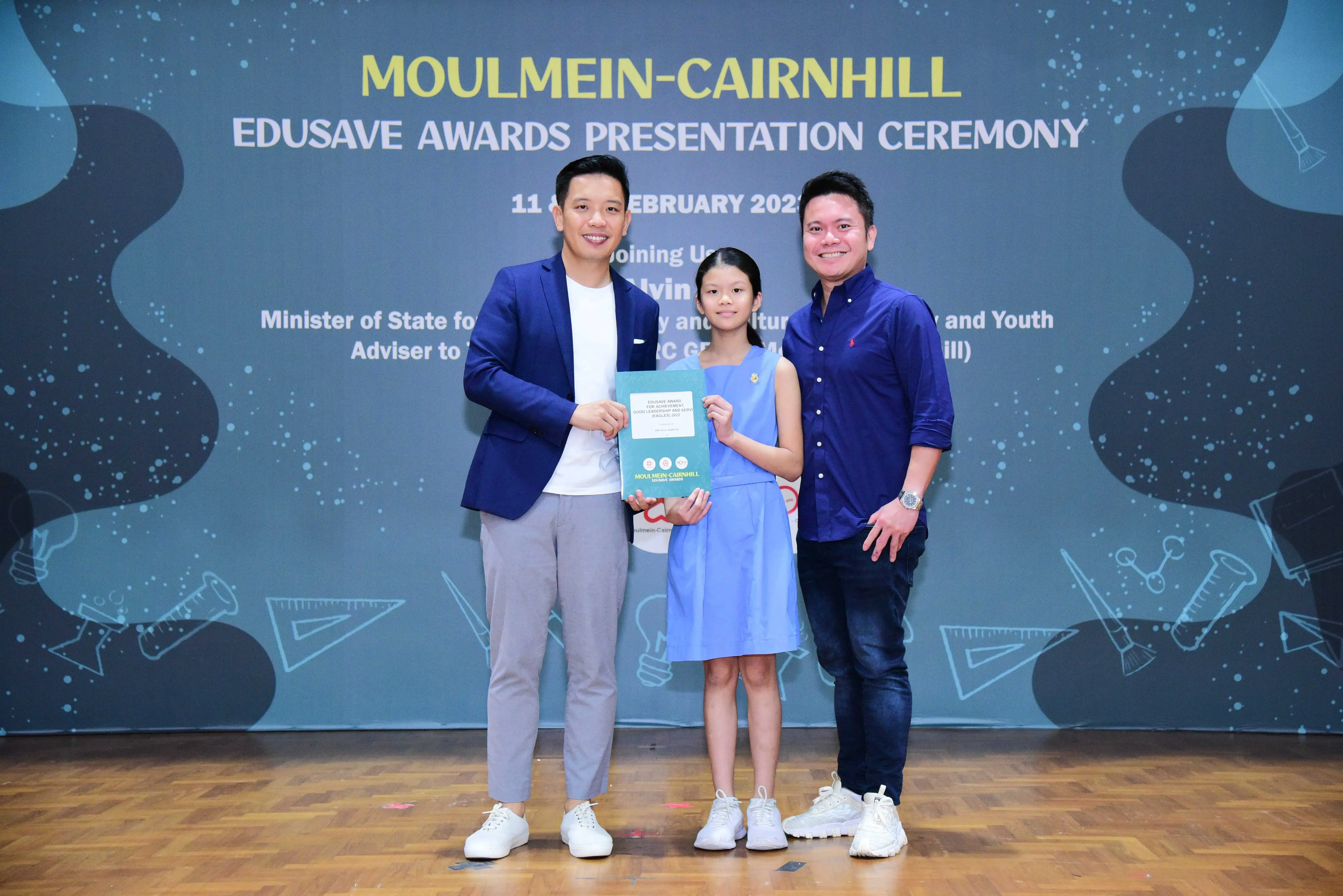 Two men and a girl holding a certificate pose at the Moulmein-Cairnhill Edusave Awards Presentation Ceremony.