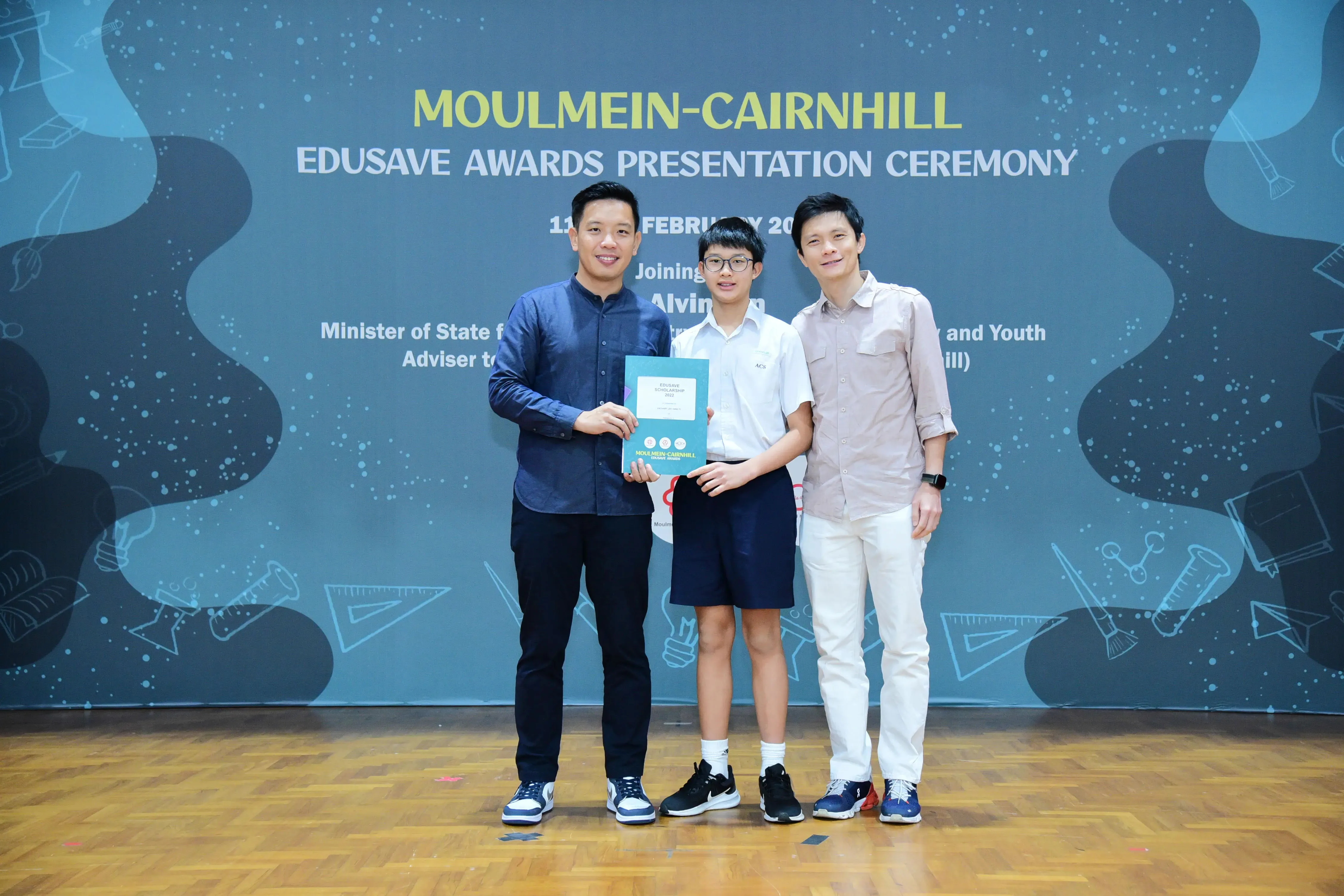 Three people stand together holding a certificate at the Moulmein-Cairnhill Edusave Awards Presentation Ceremony.