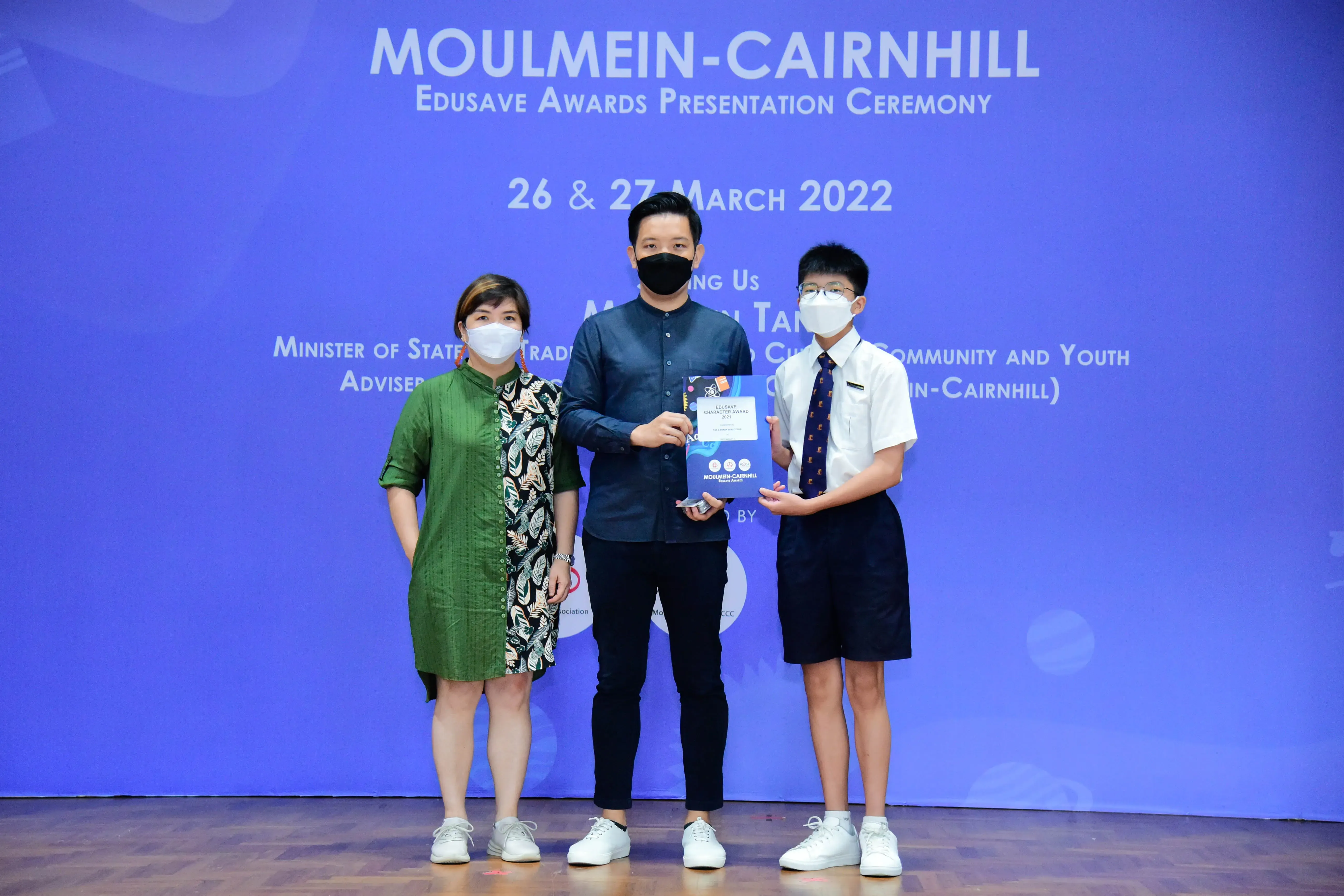 Three masked people pose with an award at the Moulmein-Cairnhill Edusave Awards Ceremony on 26-27 March 2022.