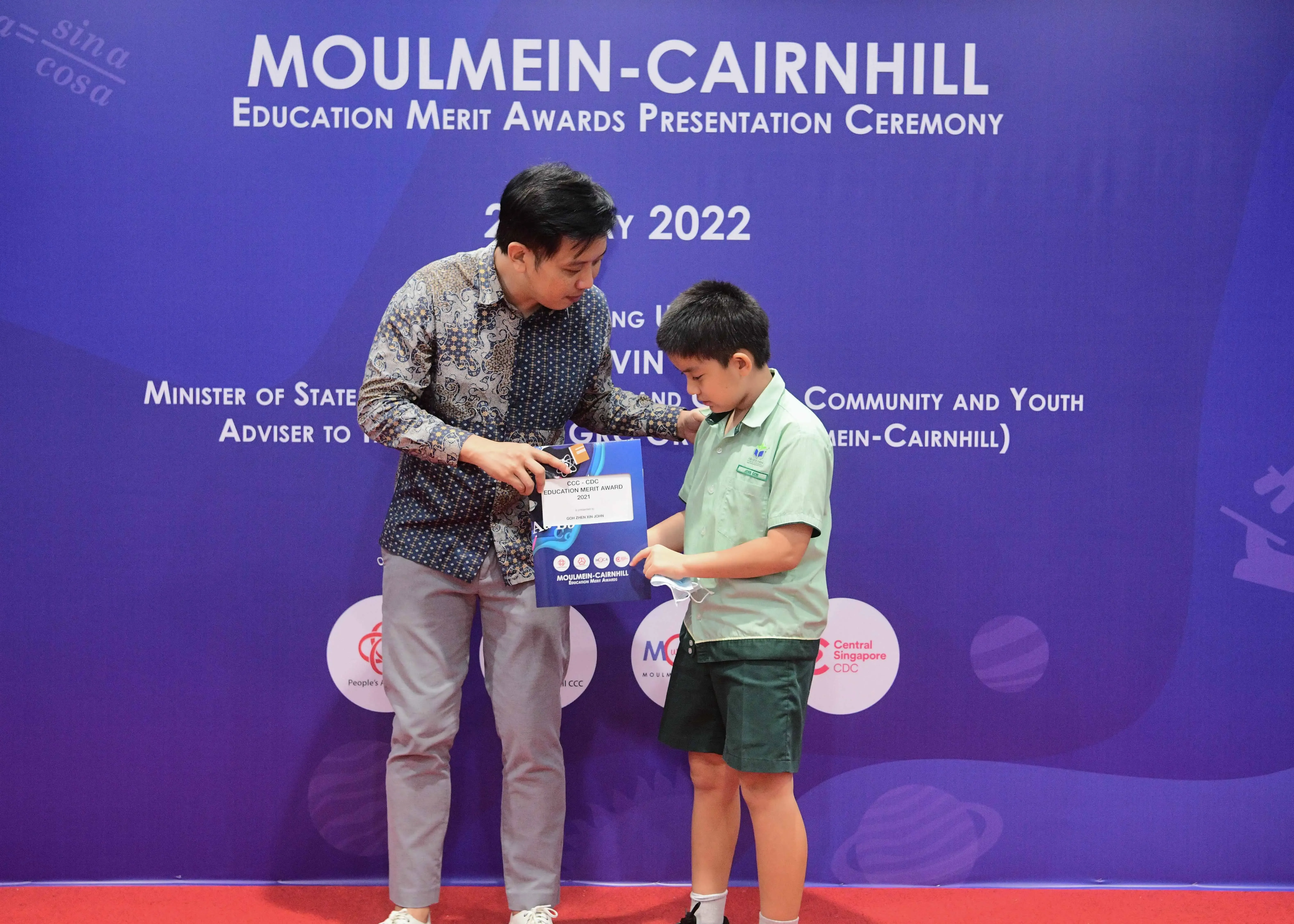 Adult man presenting an award bag to a young boy at the Moulmein-Cairnhill Education Merit Awards Ceremony 2022.