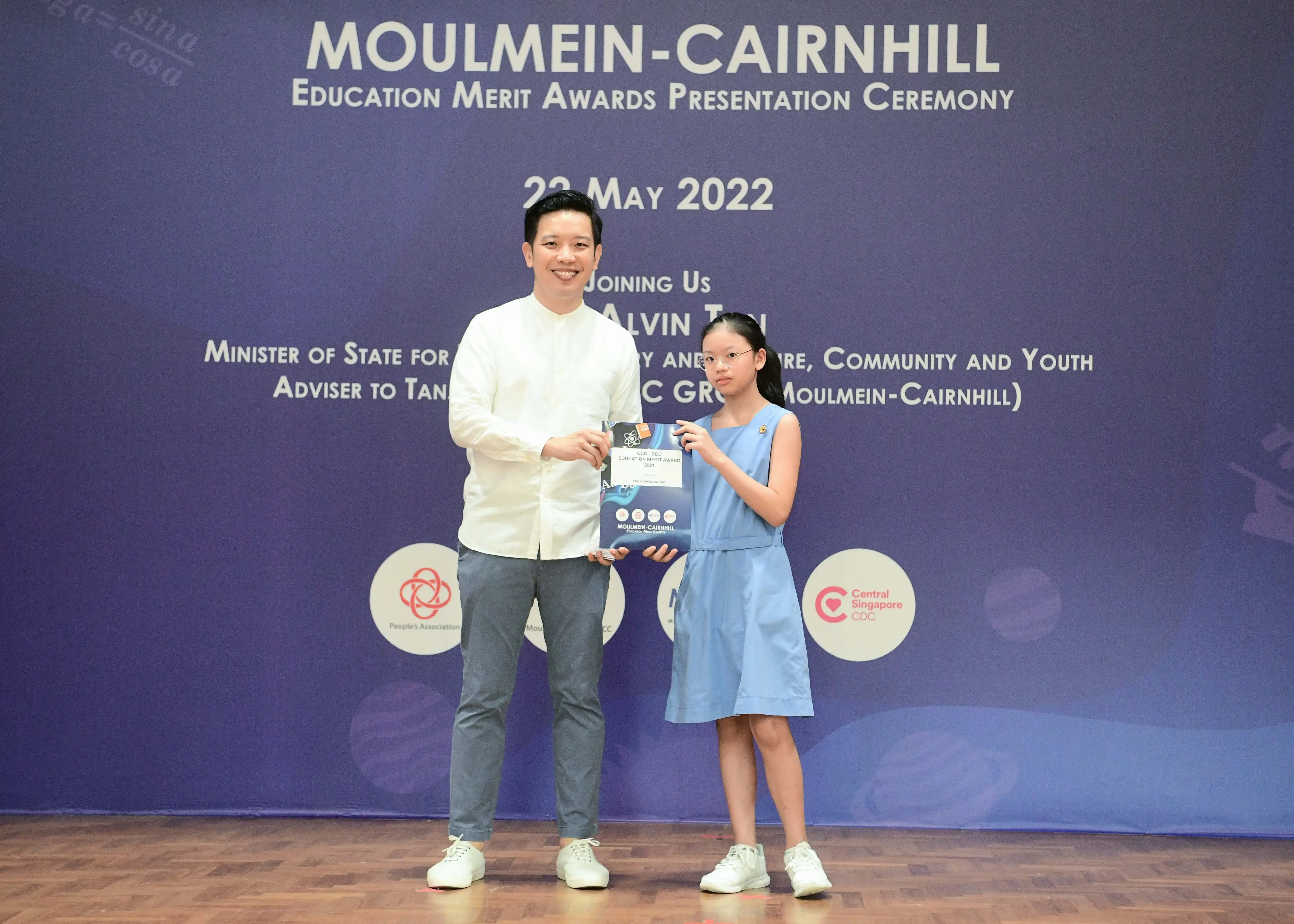 A man and a young girl hold an award certificate at the Moulmein-Cairnhill Education Merit Awards Ceremony, May 2022.