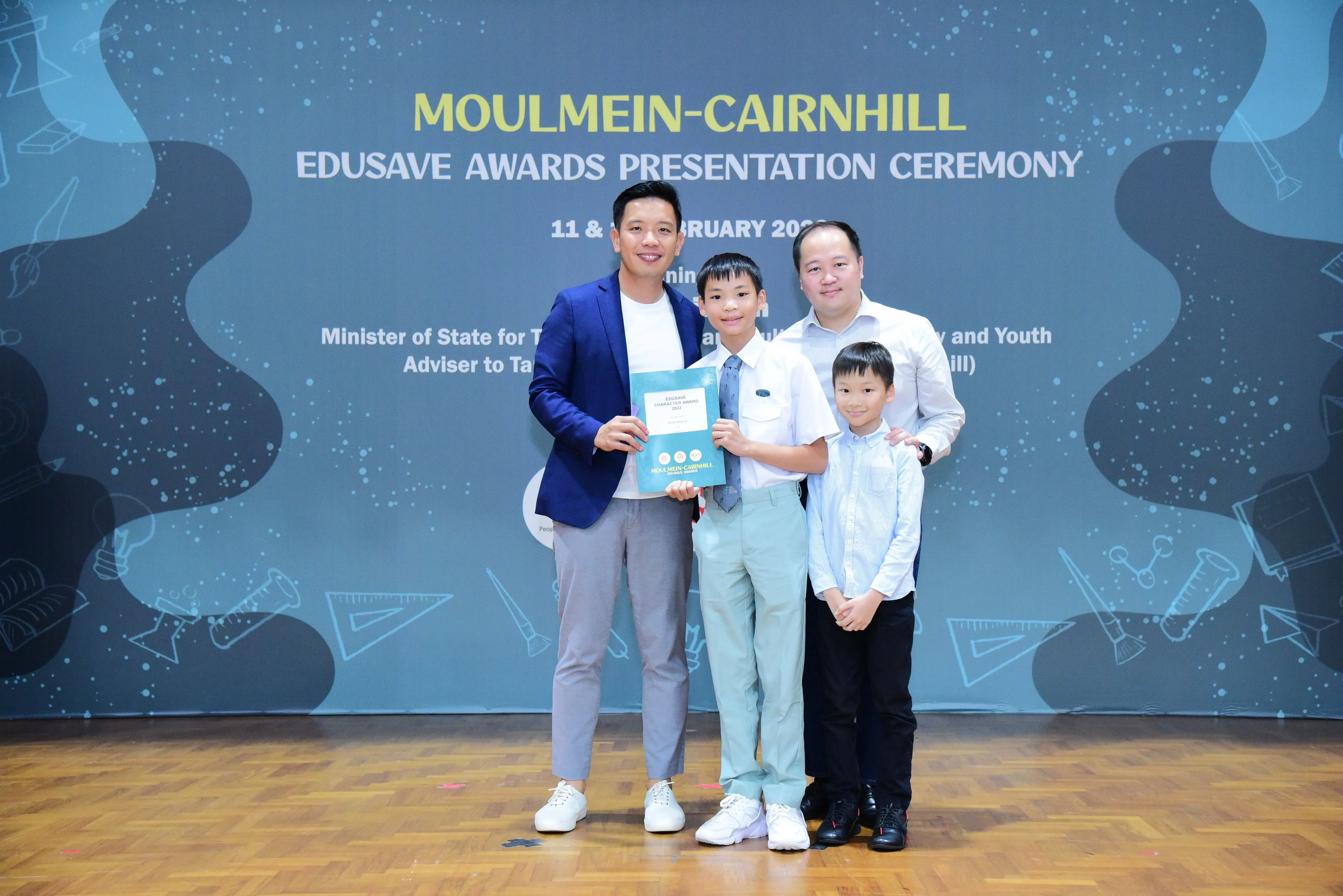Two men and two boys pose holding an award certificate at the Moulmein-Cairnhill Edusave Awards Presentation Ceremony.