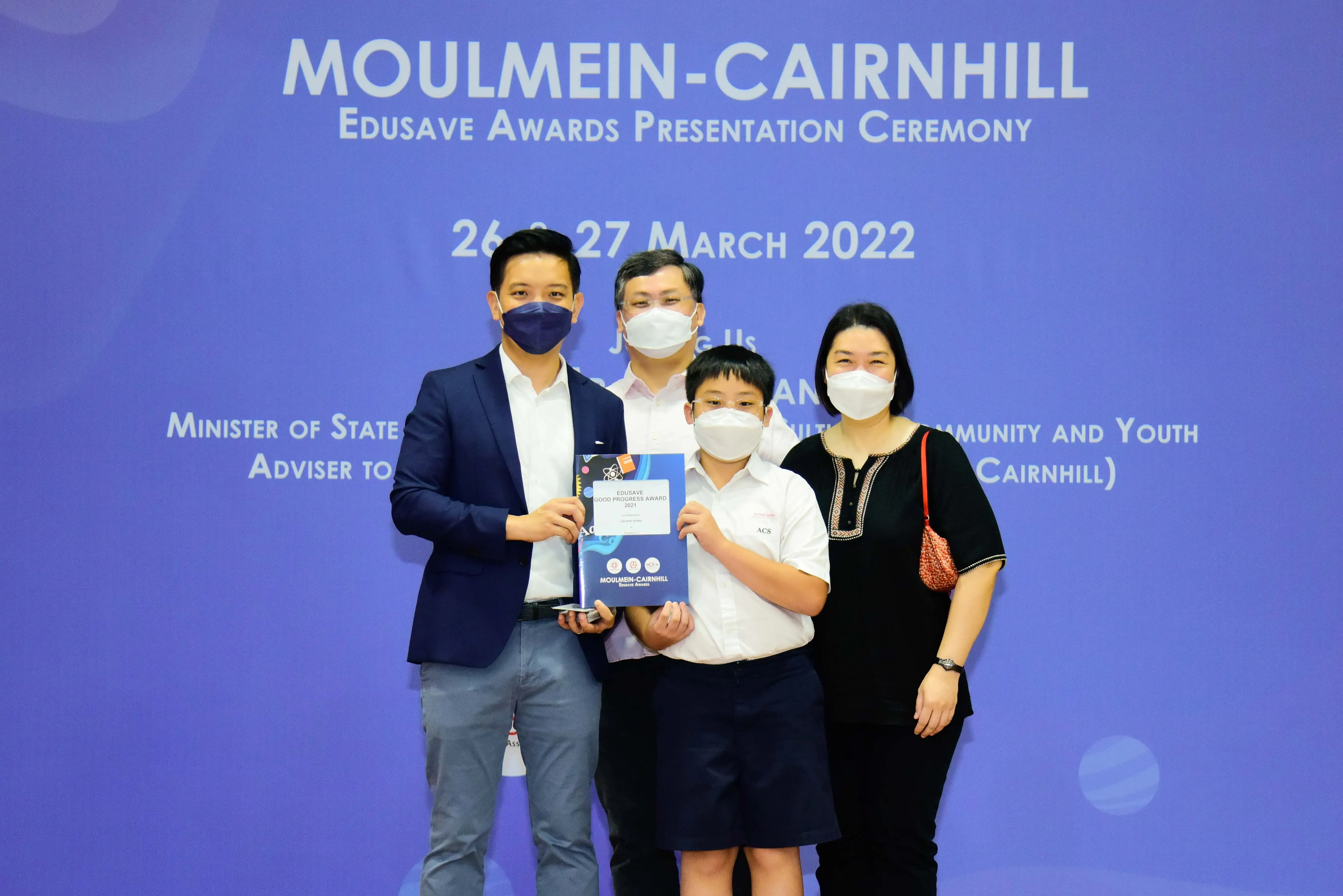 Four masked people pose with an award certificate at the Moulmein-Cairnhill Edusave Awards Ceremony, March 2022.