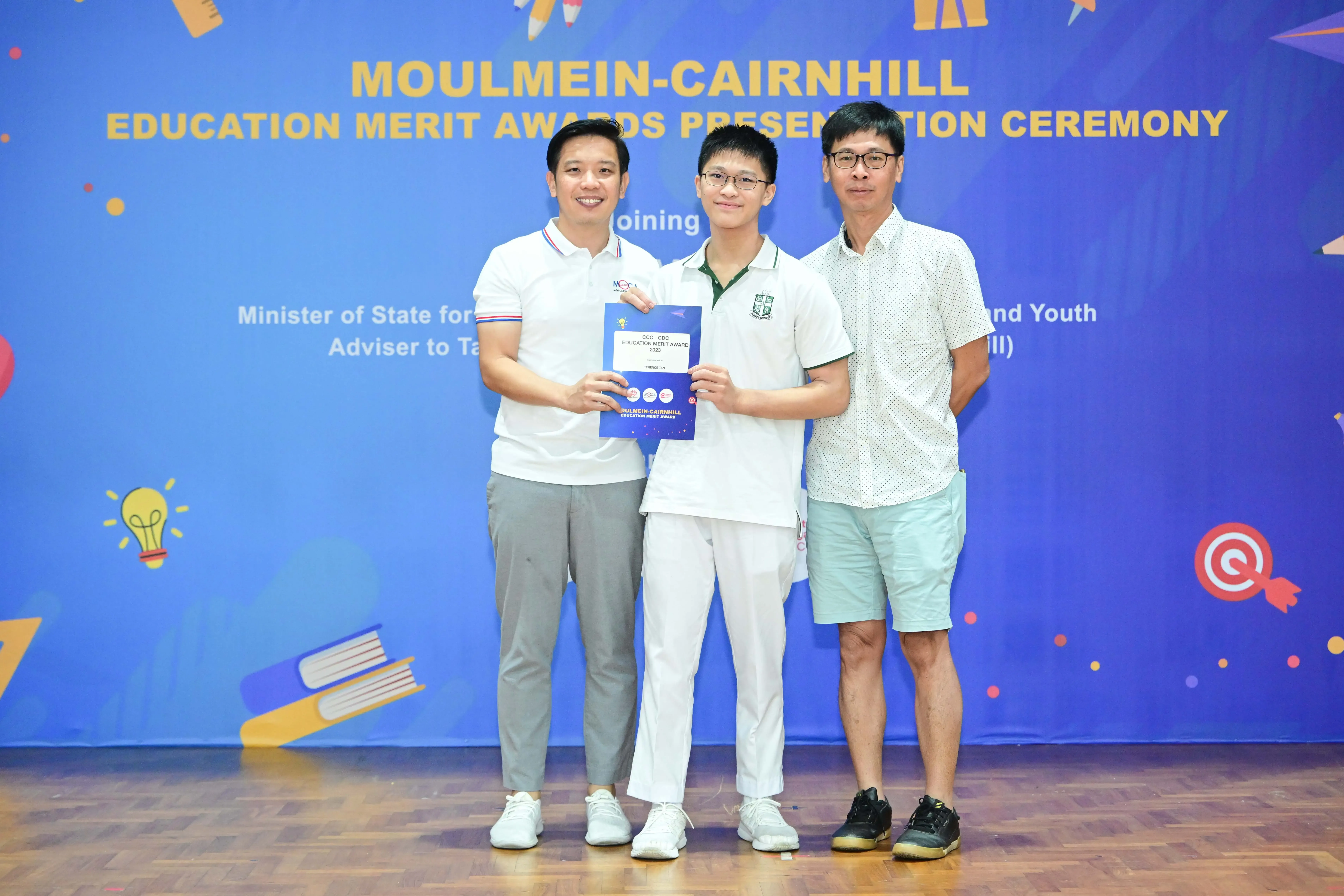 Three men pose holding an award certificate at the Moulmein-Cairnhill Education Merit Awards ceremony.