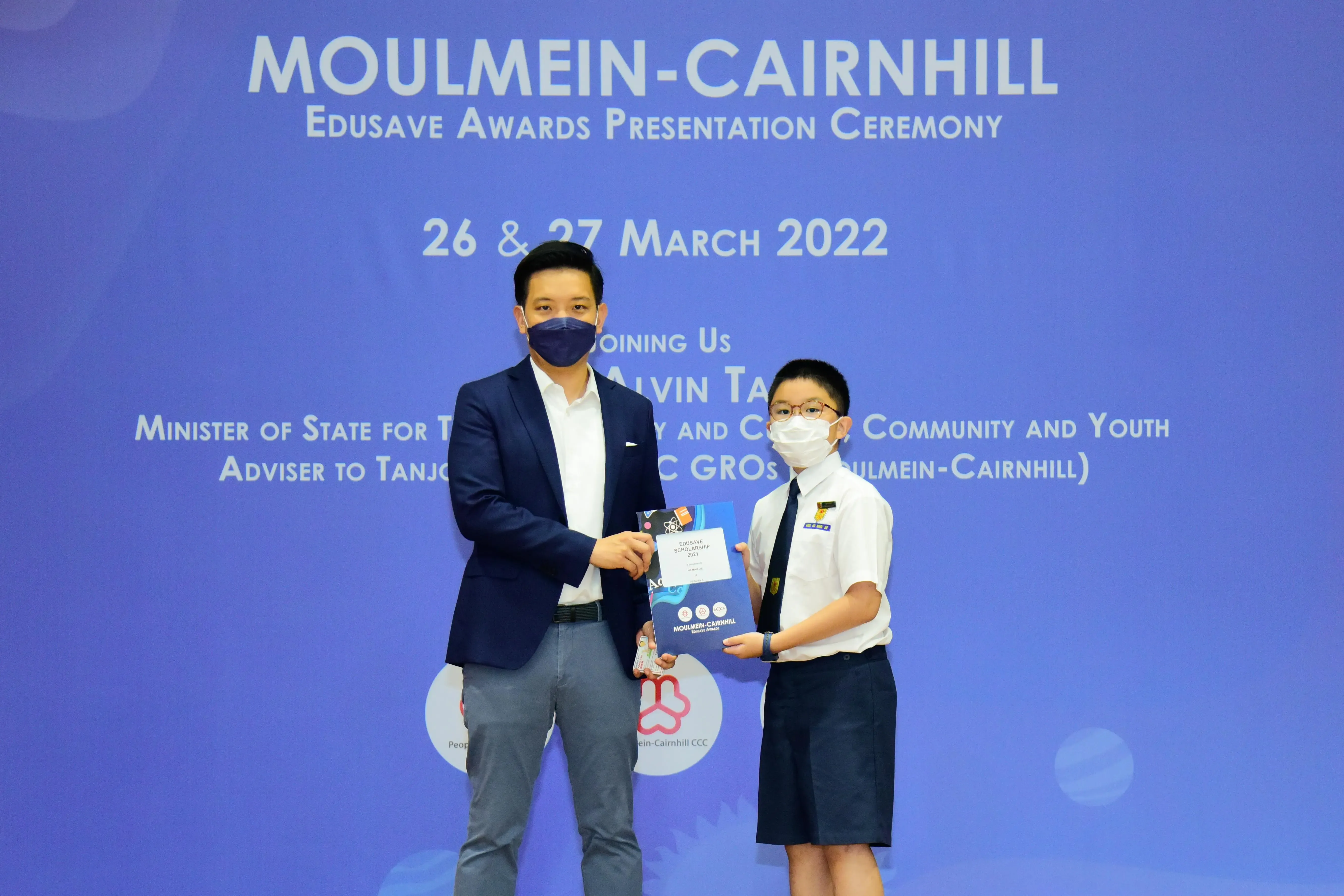 An adult and a uniformed student hold an award together at the Moulmein-Cairnhill Edusave Awards Ceremony, March 2022.