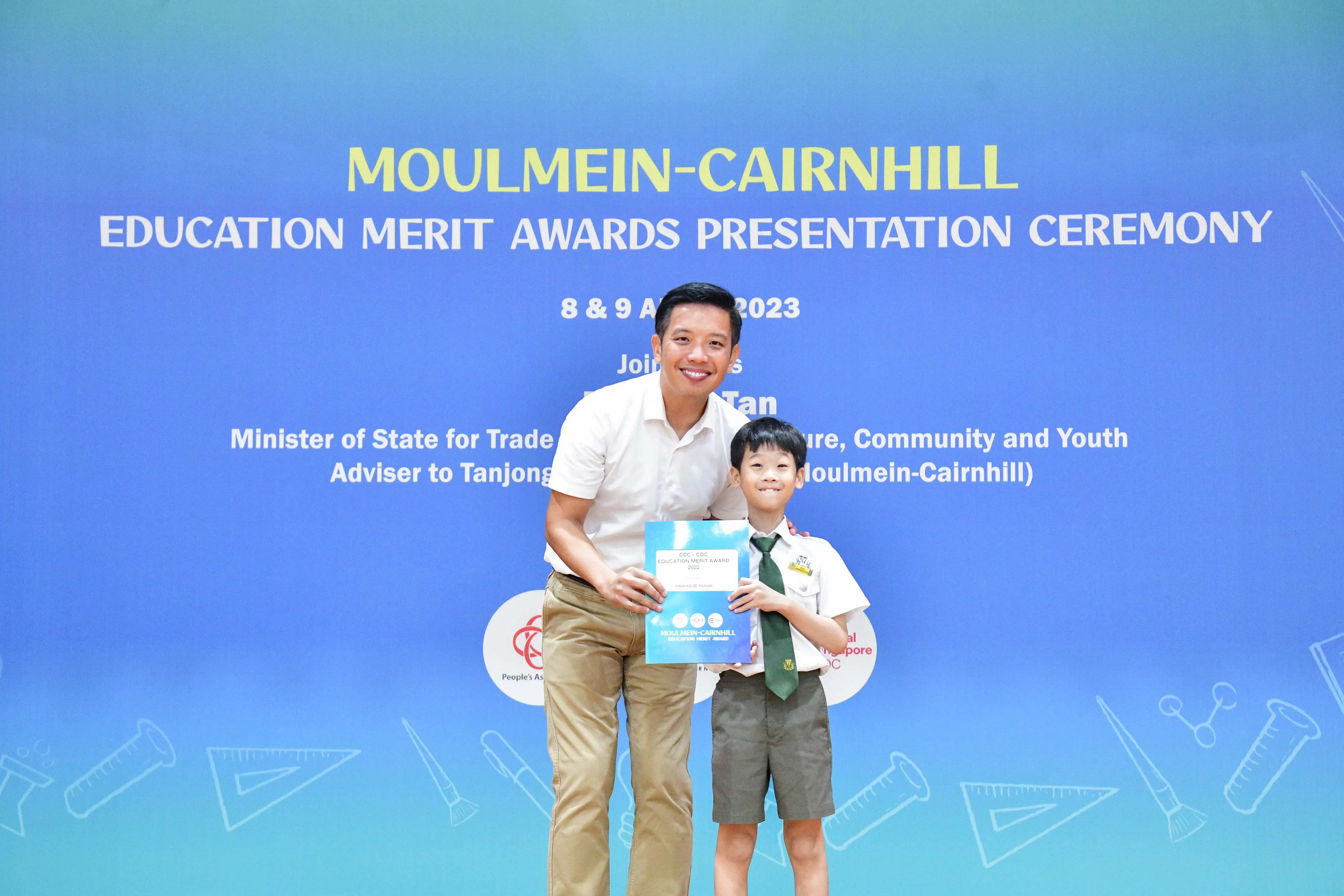 A man and a young boy in school uniform hold a certificate at the Moulmein-Cairnhill Education Merit Awards 2023.