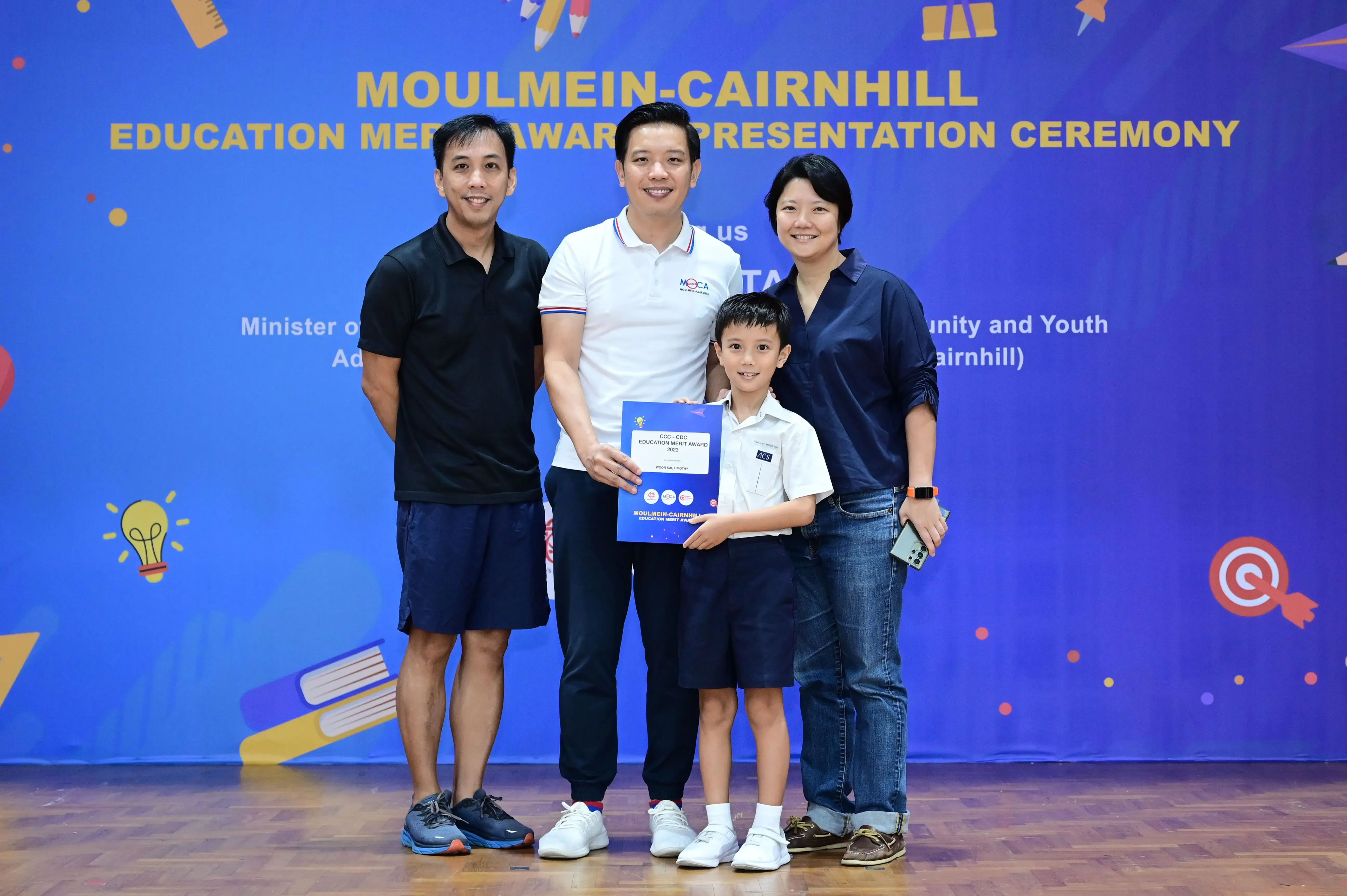 Three adults and a young boy pose with an award certificate at the Moulmein-Cairnhill Education Merit Award Ceremony.