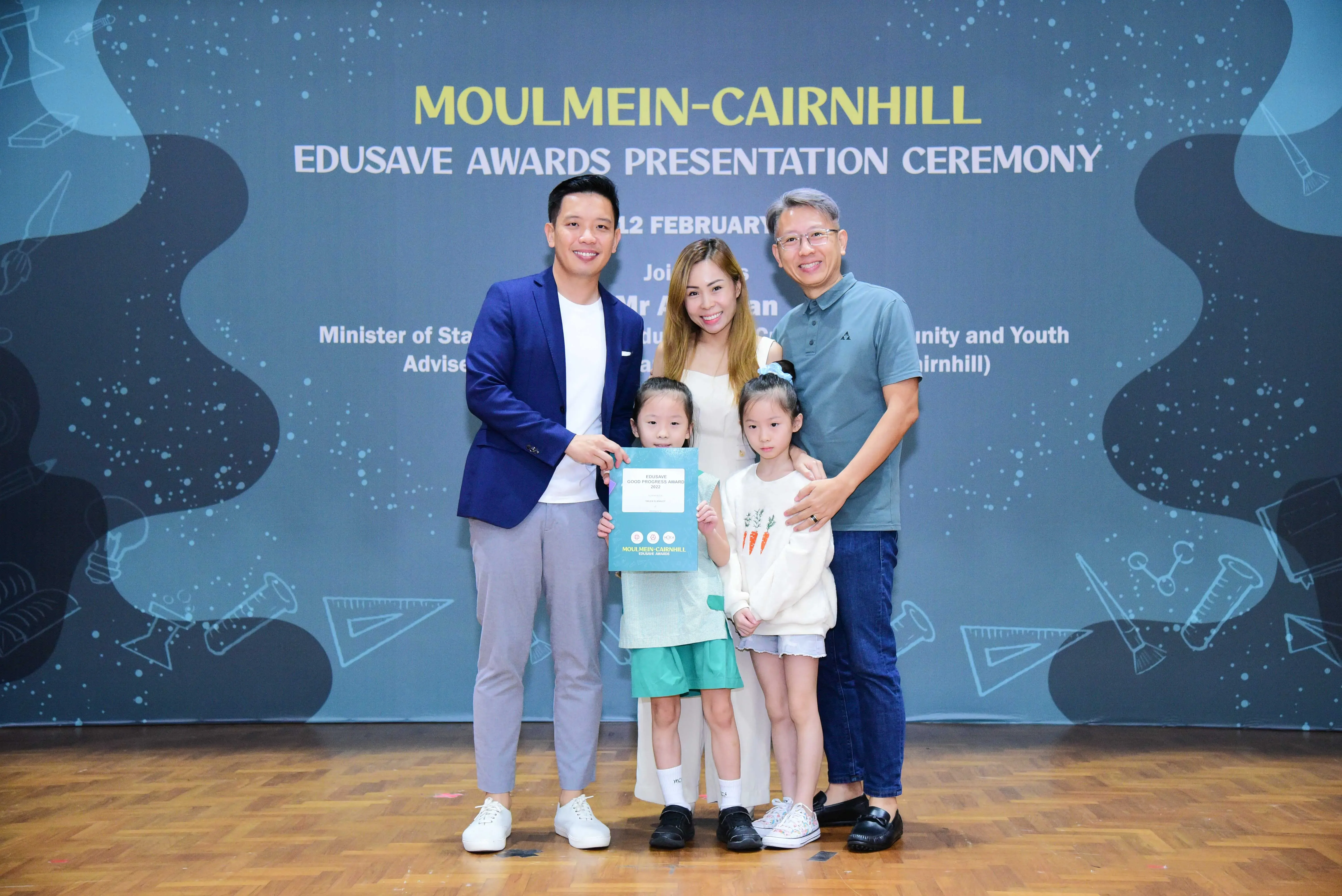Five people pose at the Moulmein-Cairnhill Edusave Awards Presentation Ceremony, with a child holding an award certificate.