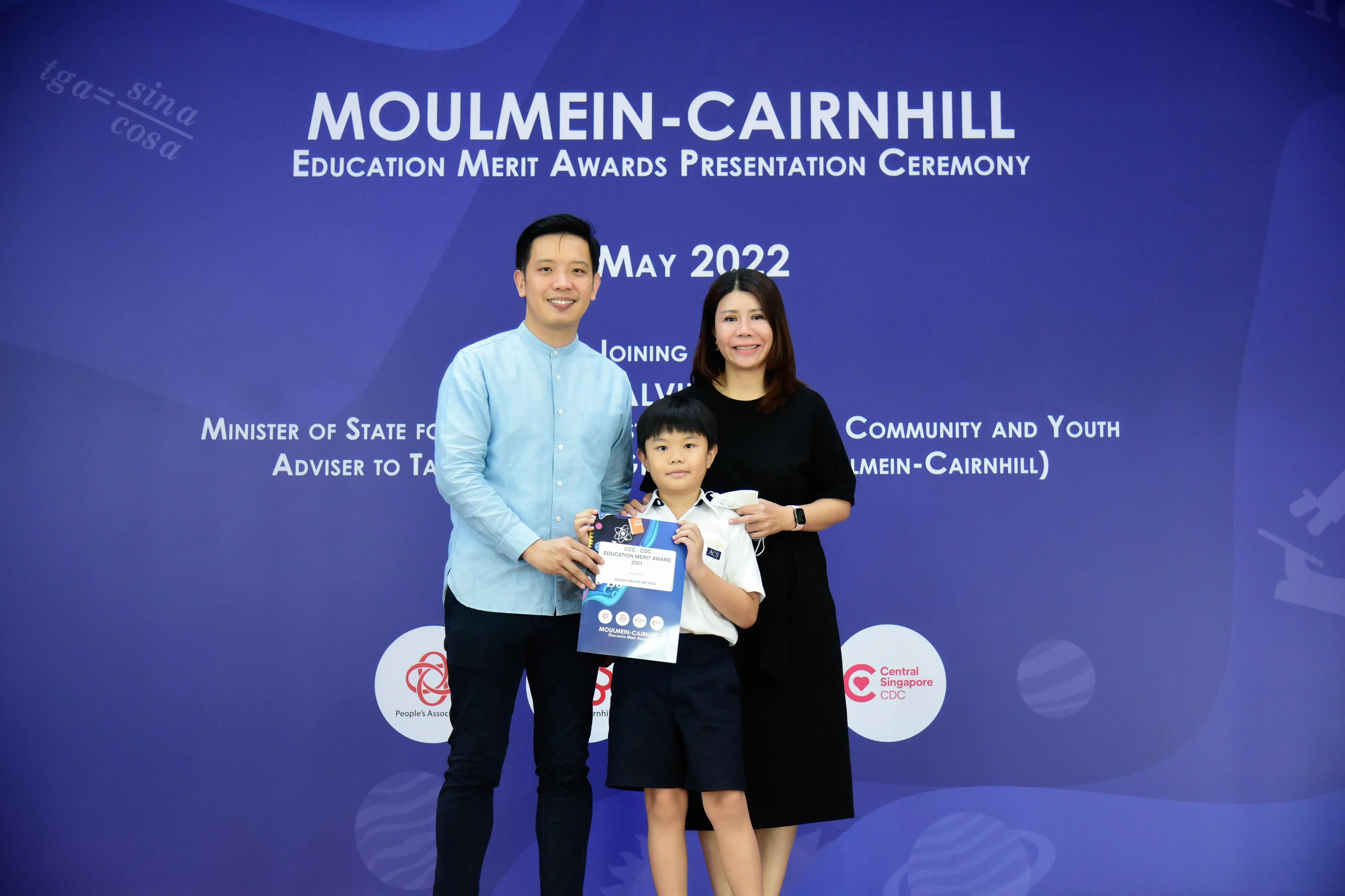 Two adults and a young boy holding an award certificate pose at the Moulmein-Cairnhill Education Merit Awards May 2022.