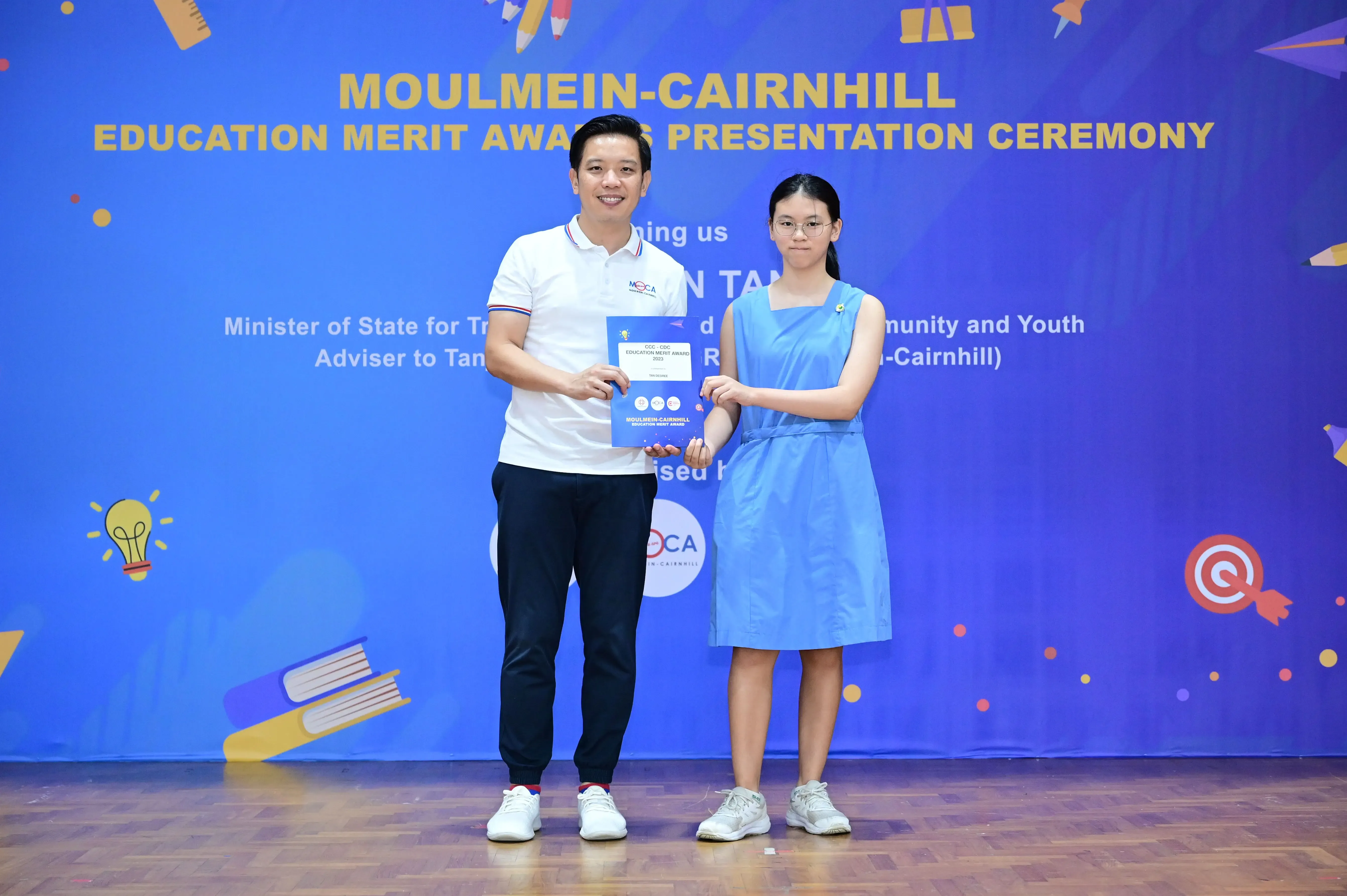 A man and a girl hold an award certificate at the Moulmein-Cairnhill Education Merit Awards Presentation Ceremony.
