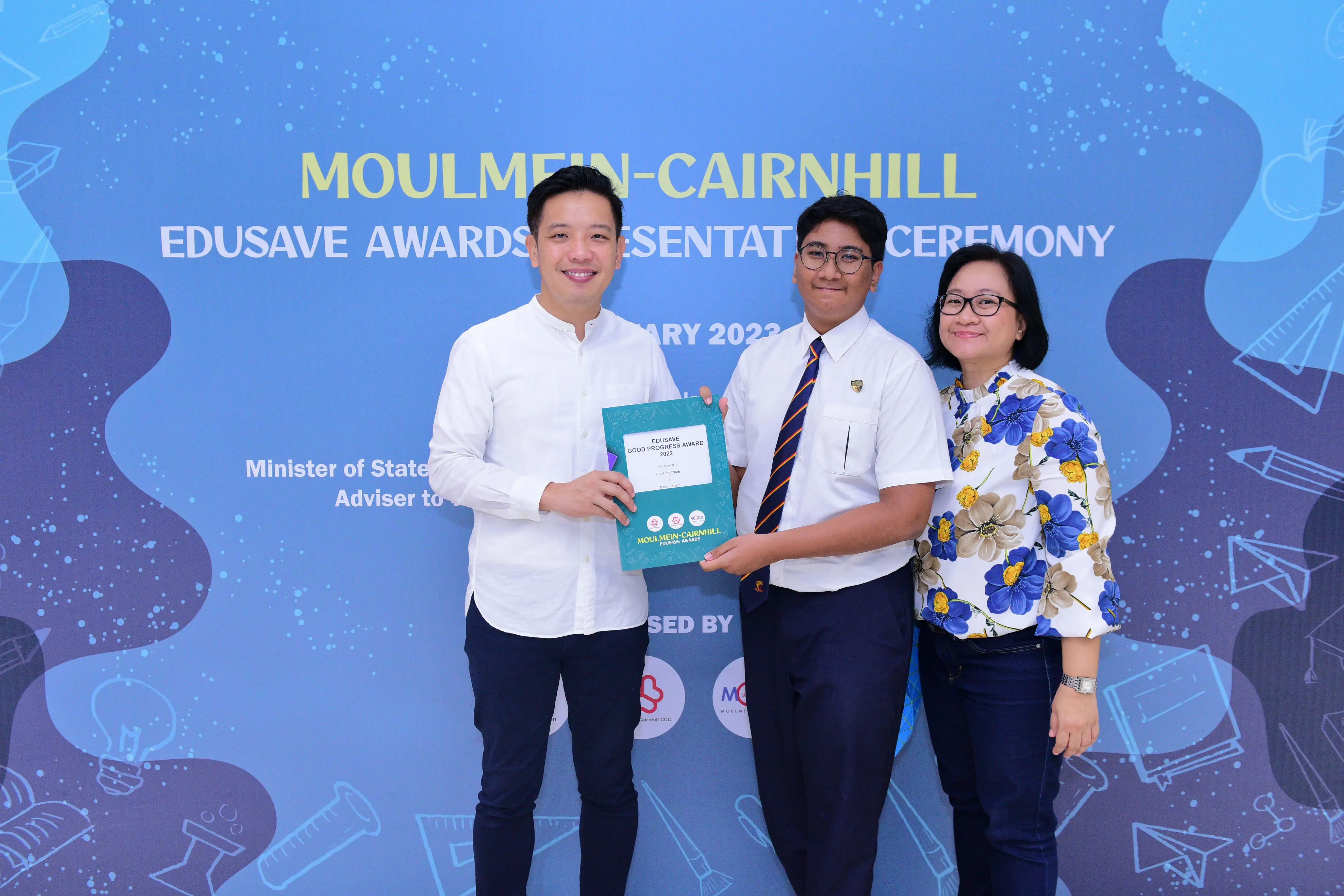 Three people pose together holding an Edusave Good Progress Award certificate at the Moulmein-Cairnhill Awards Ceremony.