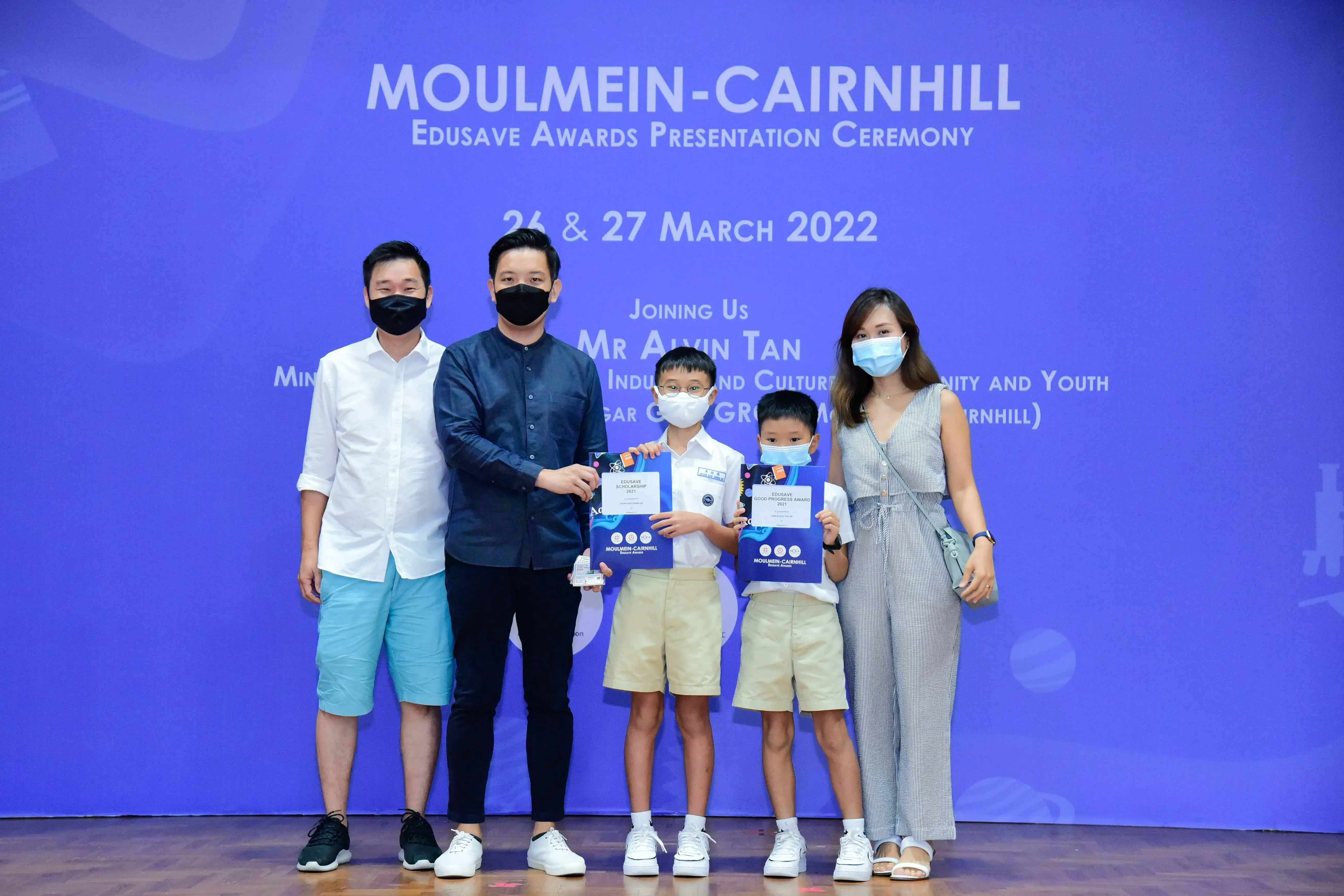 Two adults and two young boys wearing masks pose with award certificates at the Moulmein-Cairnhill Edusave ceremony, March 2022.