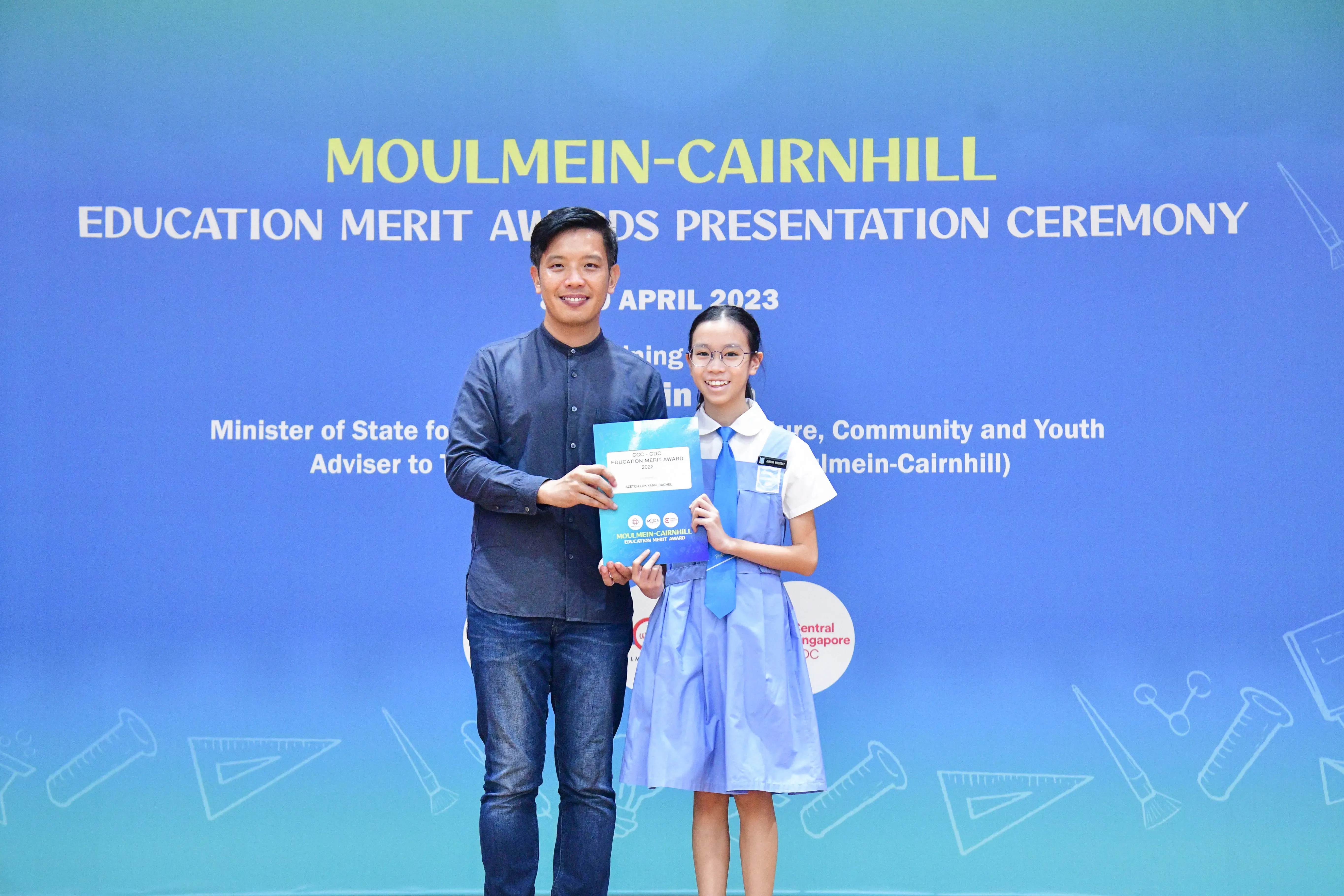 A man and a young girl in school uniform hold an award certificate at the Moulmein-Cairnhill Education Merit Awards 2023.