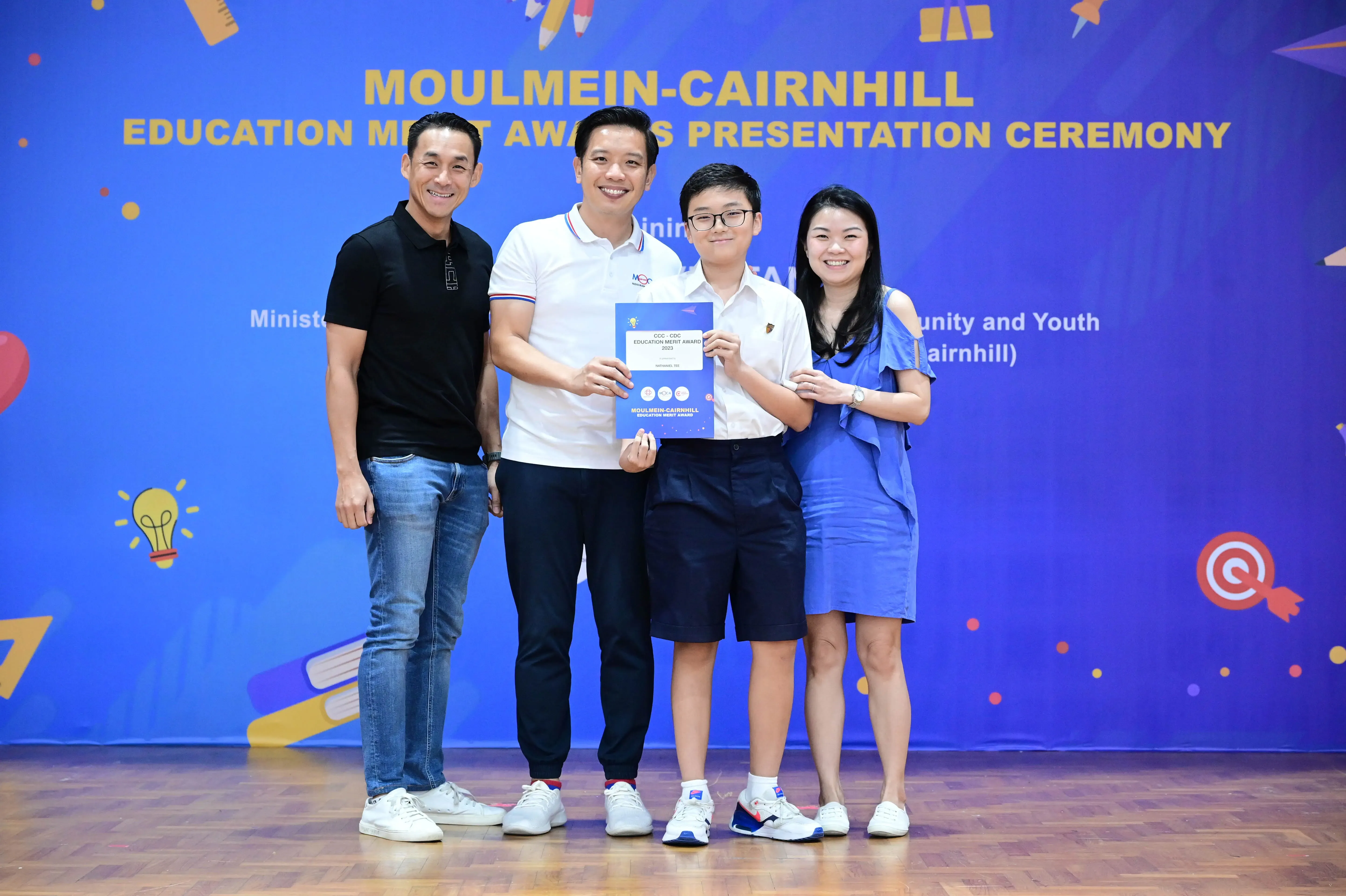 Four people pose holding an award certificate at the Moulmein-Cairnhill Education Merit Awards Presentation Ceremony.