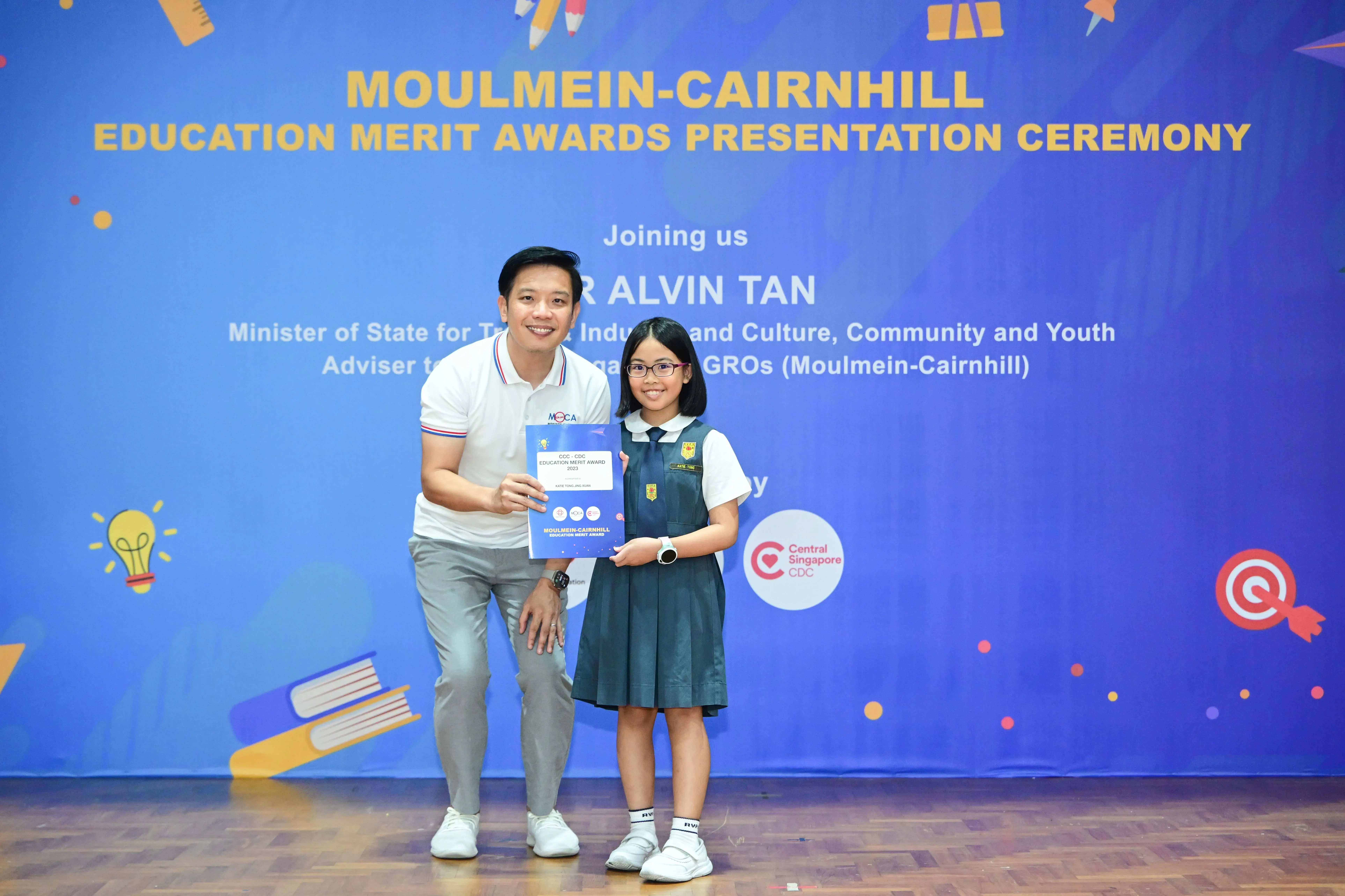 A man and a young girl in school uniform hold a certificate at the Moulmein-Cairnhill Education Merit Awards ceremony.