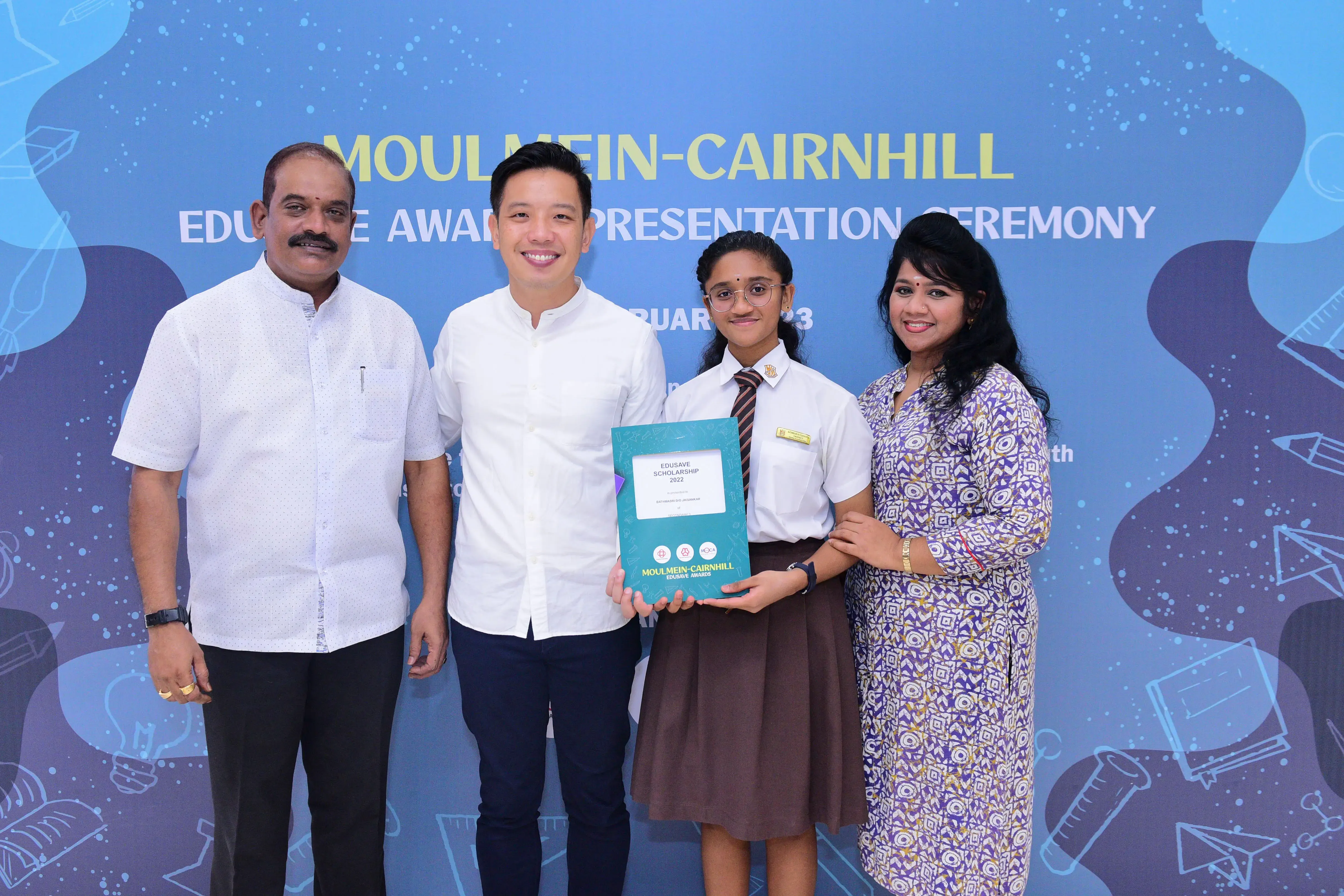 Four people pose at the Moulmein-Cairnhill Edusave Awards Presentation Ceremony, with a student holding a certificate.