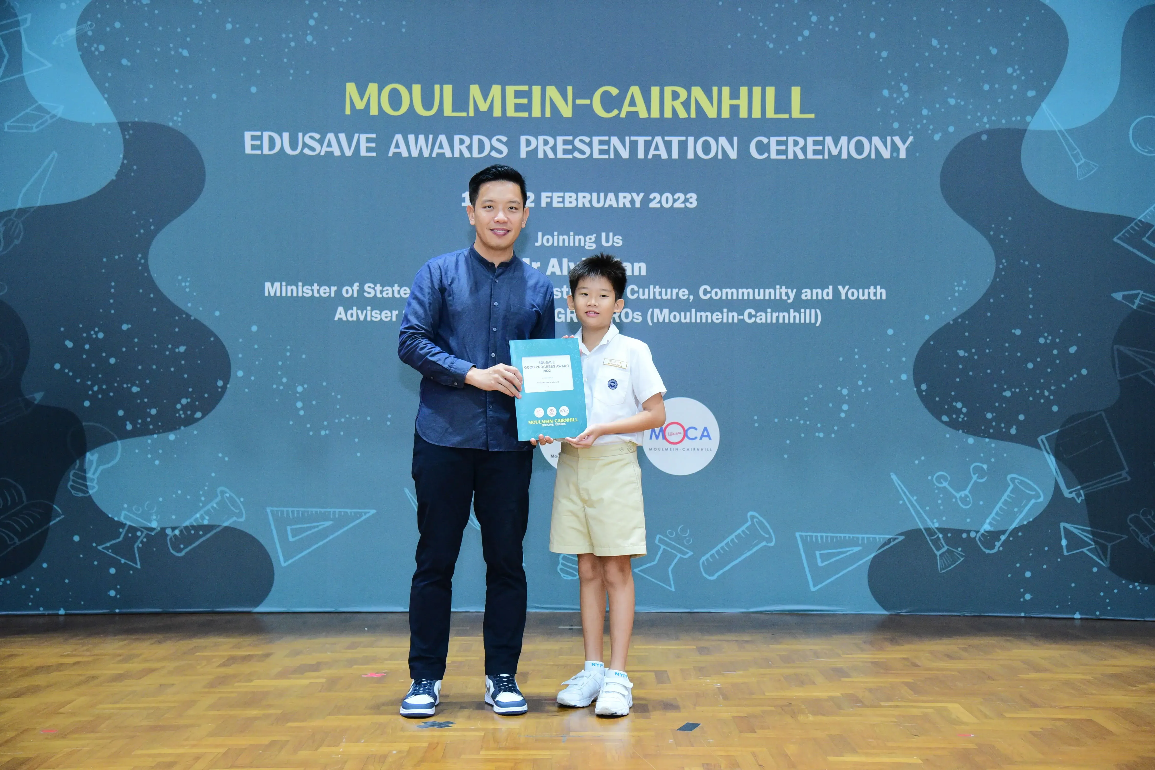 A man and a young boy hold an award together at the Moulmein-Cairnhill Edusave Awards Ceremony, February 2023.