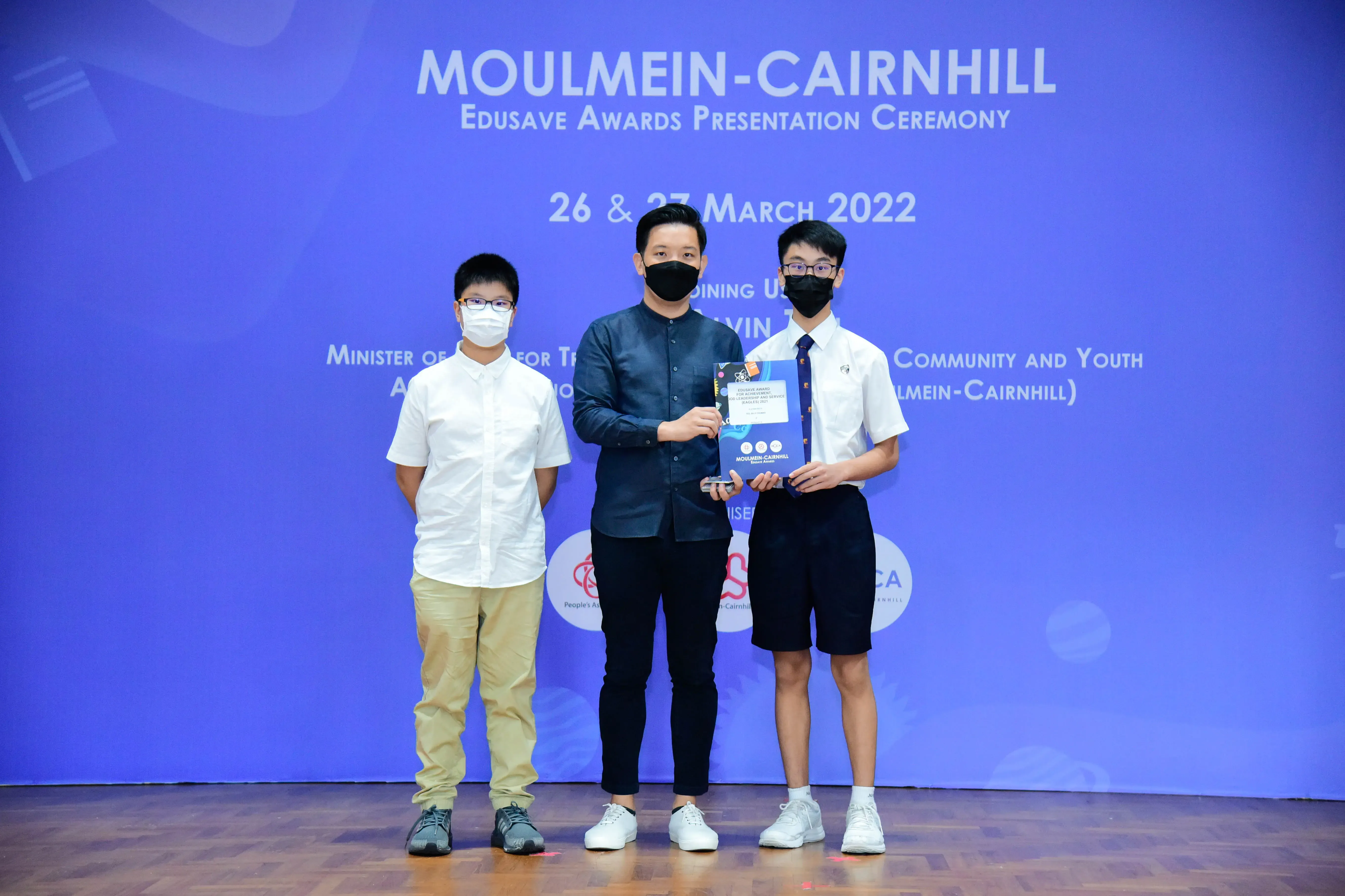 Three masked individuals stand on a stage at the Moulmein-Cairnhill Edusave Awards Ceremony, March 2022.