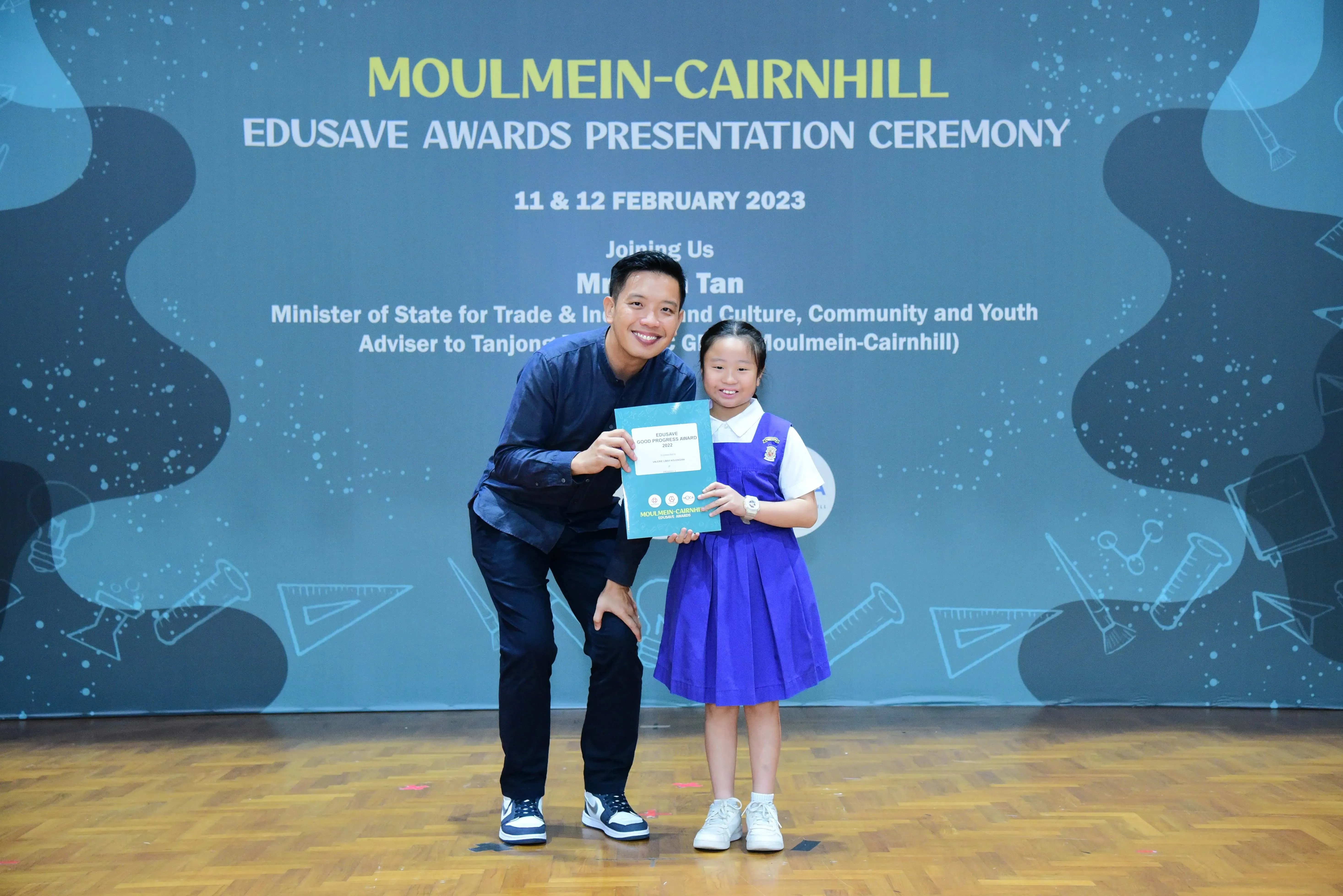 A man and a young girl in school uniform hold a certificate at the Moulmein-Cairnhill Edusave Awards Ceremony 2023.