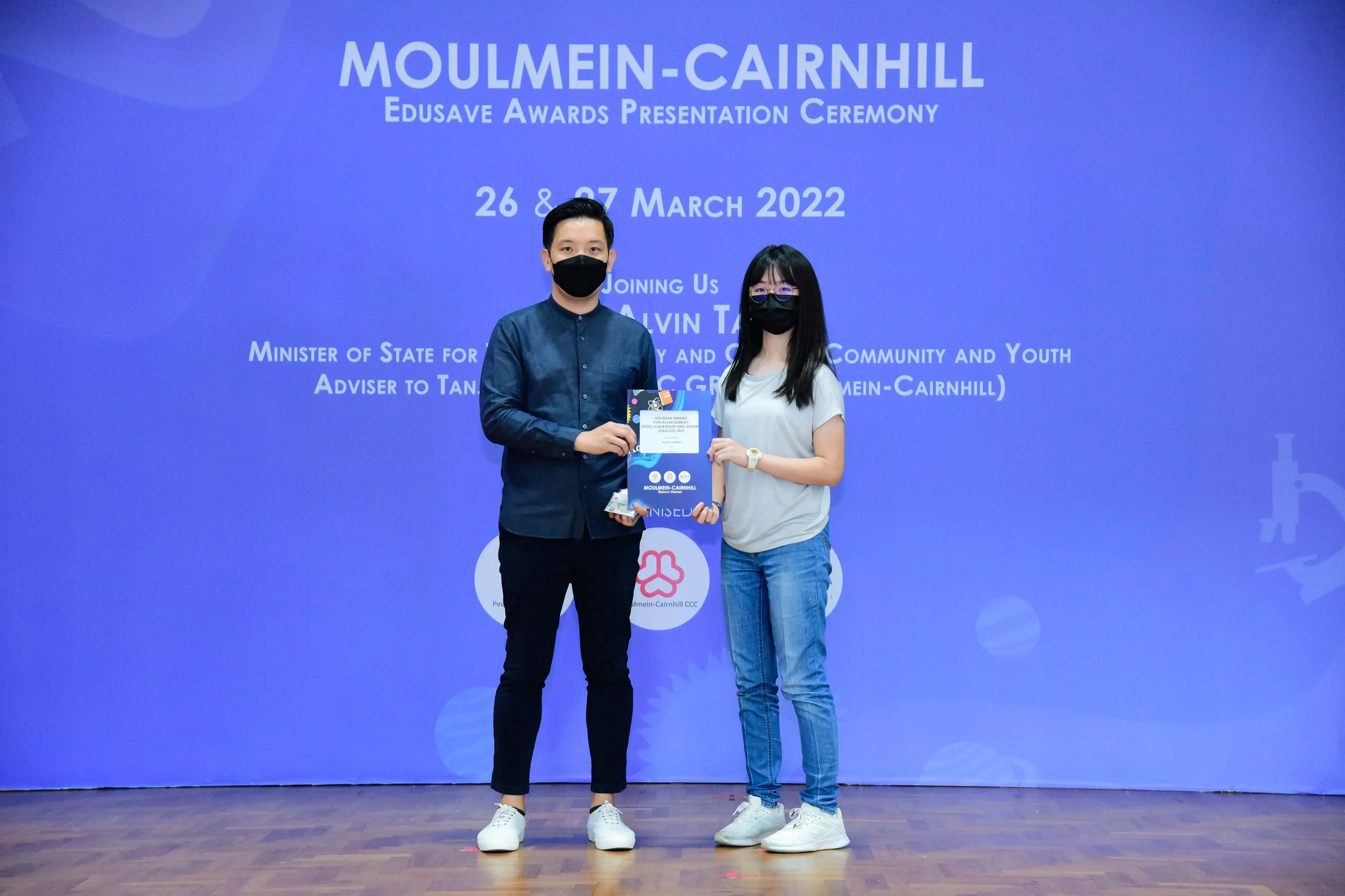 Two masked people hold an award certificate at the Moulmein-Cairnhill Edusave Awards Ceremony, March 2022.