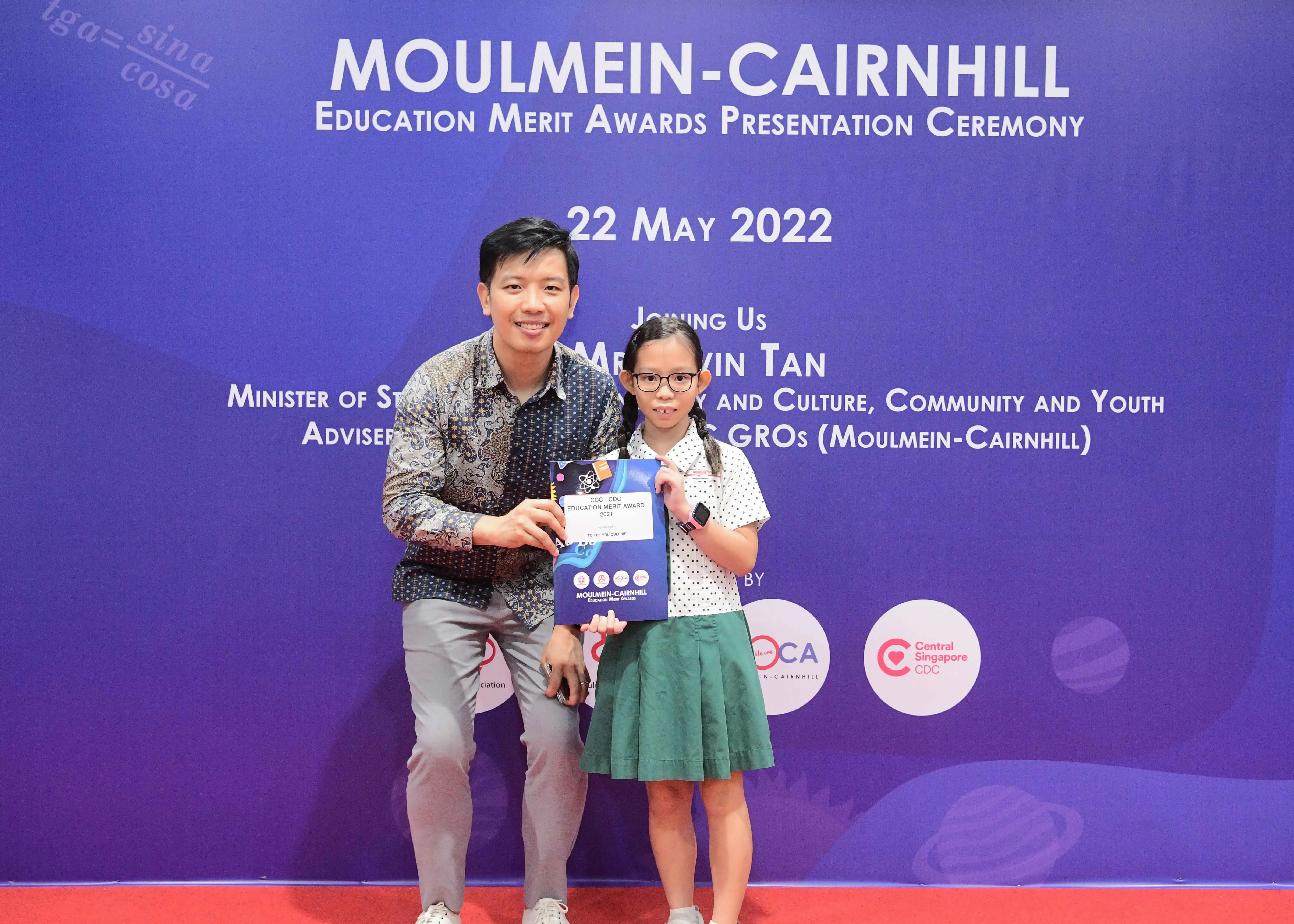 A man and a young girl pose together holding an award certificate at the Moulmein-Cairnhill Education Merit Awards ceremony.