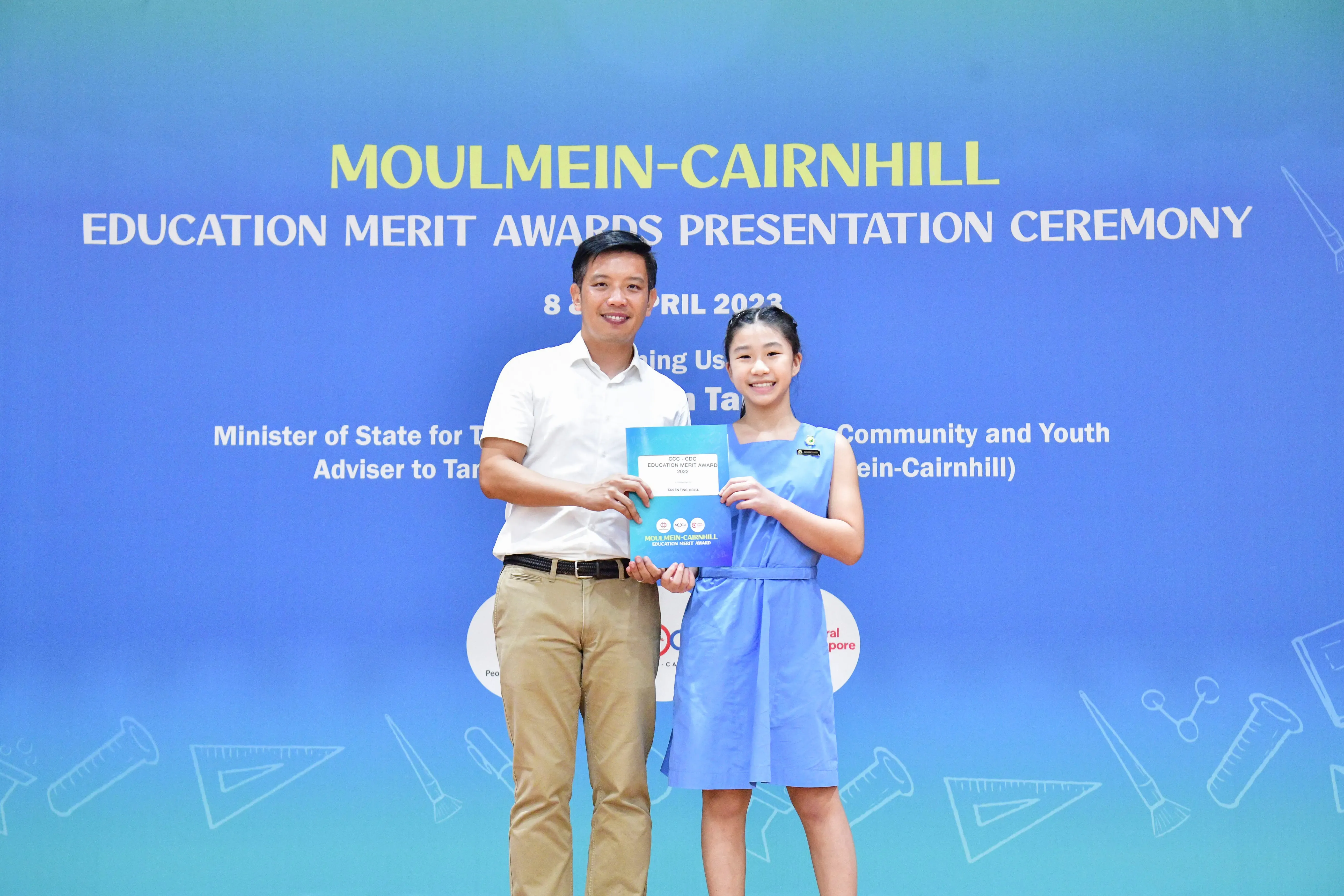 A man and a young girl hold a certificate together at the Moulmein-Cairnhill Education Merit Awards Ceremony 2023.