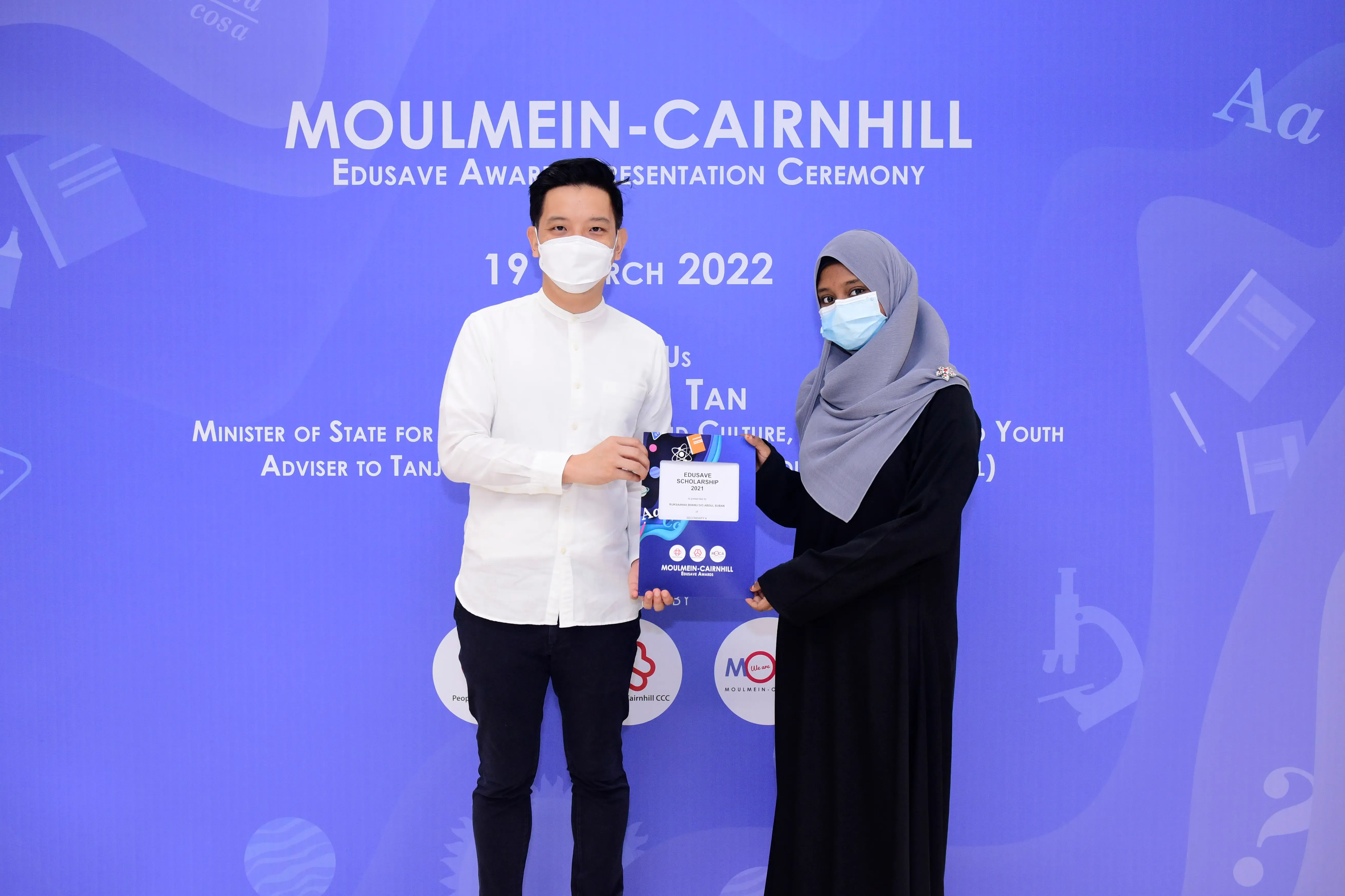 Two masked people hold an Edusave Scholarship folder at the Moulmein-Cairnhill Award Ceremony on 19 March 2022.