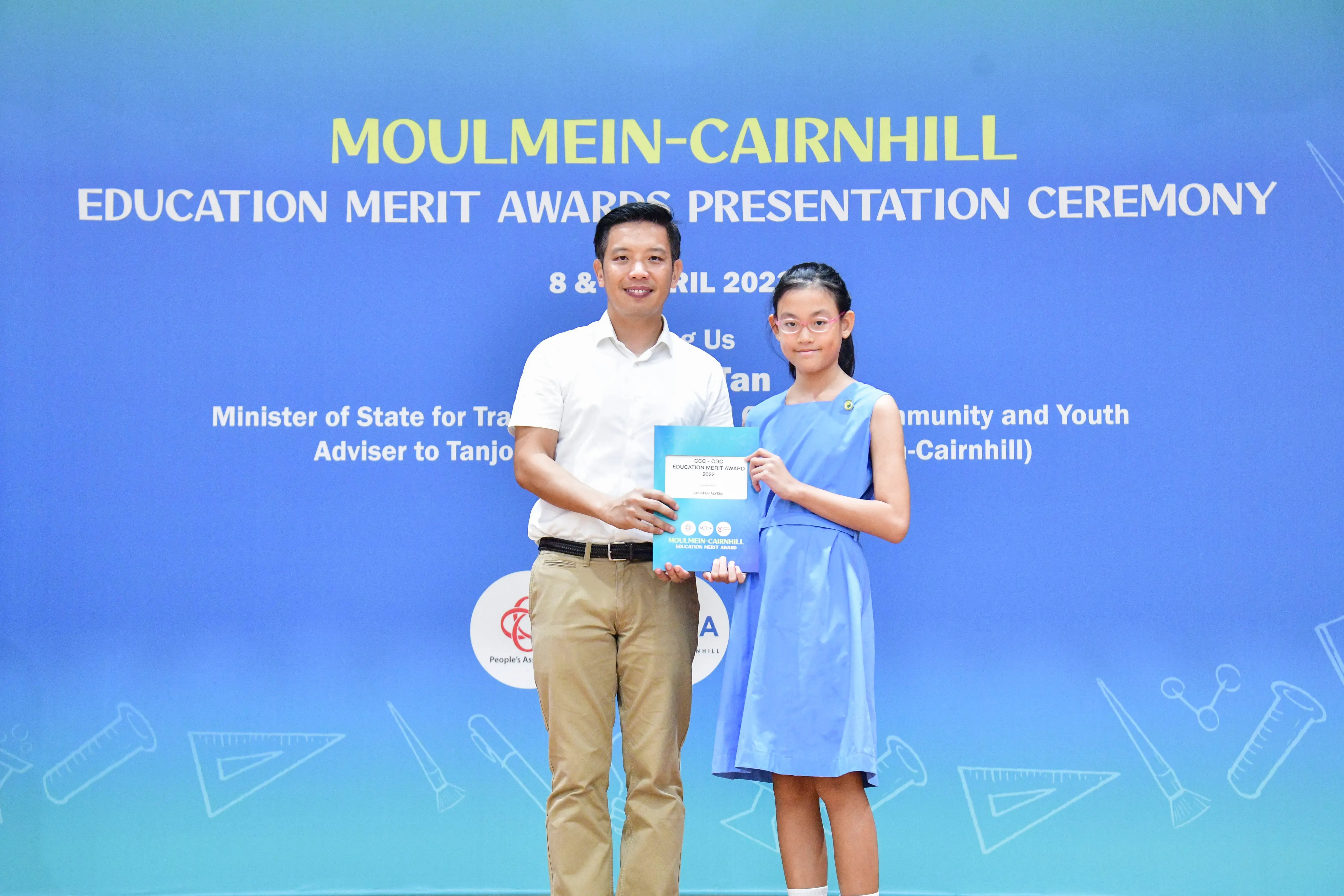 A man and a young girl hold an award certificate at the Moulmein-Cairnhill Education Merit Awards Ceremony.