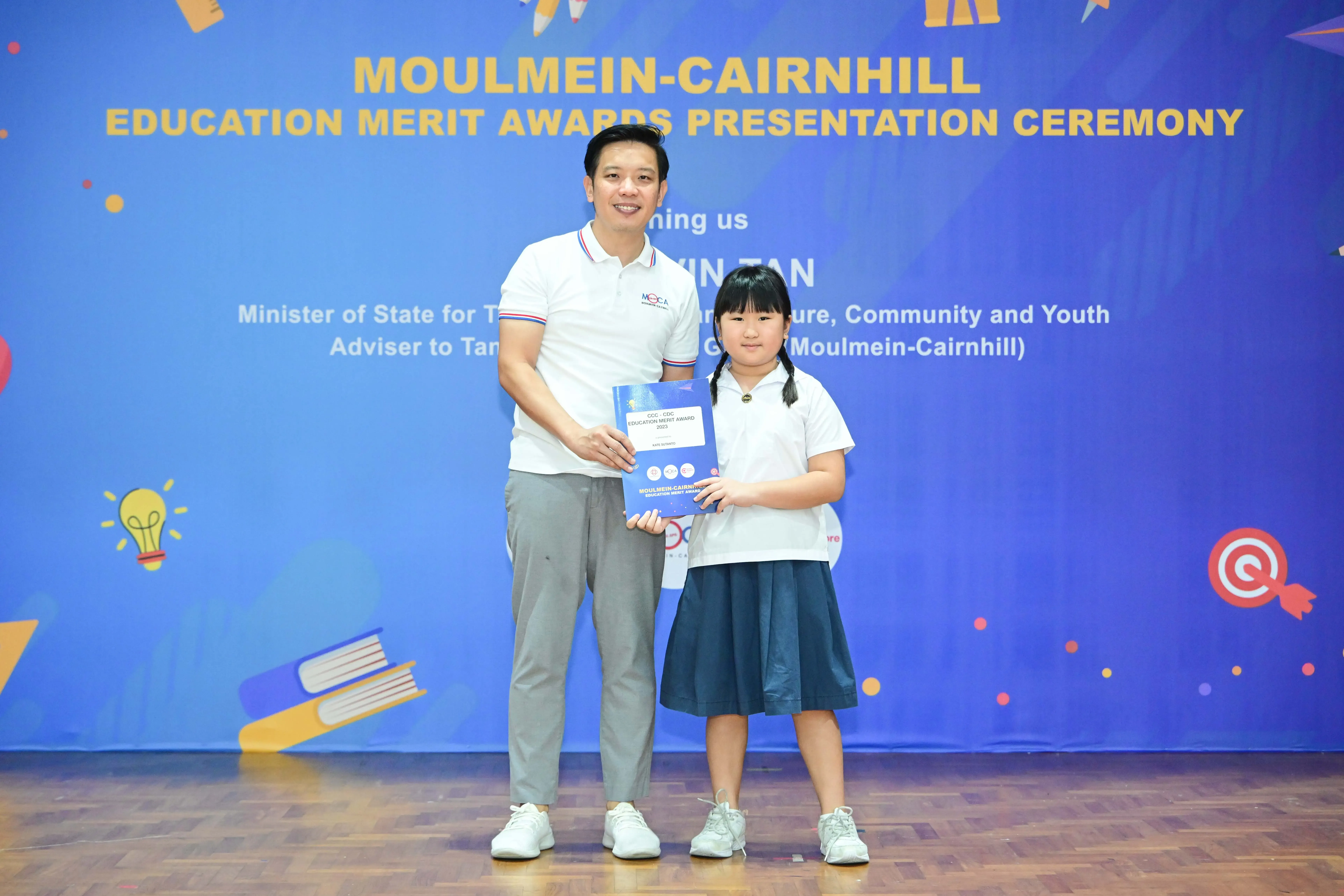 A man and a young girl hold an award certificate at the Moulmein-Cairnhill Education Merit Awards Presentation Ceremony.