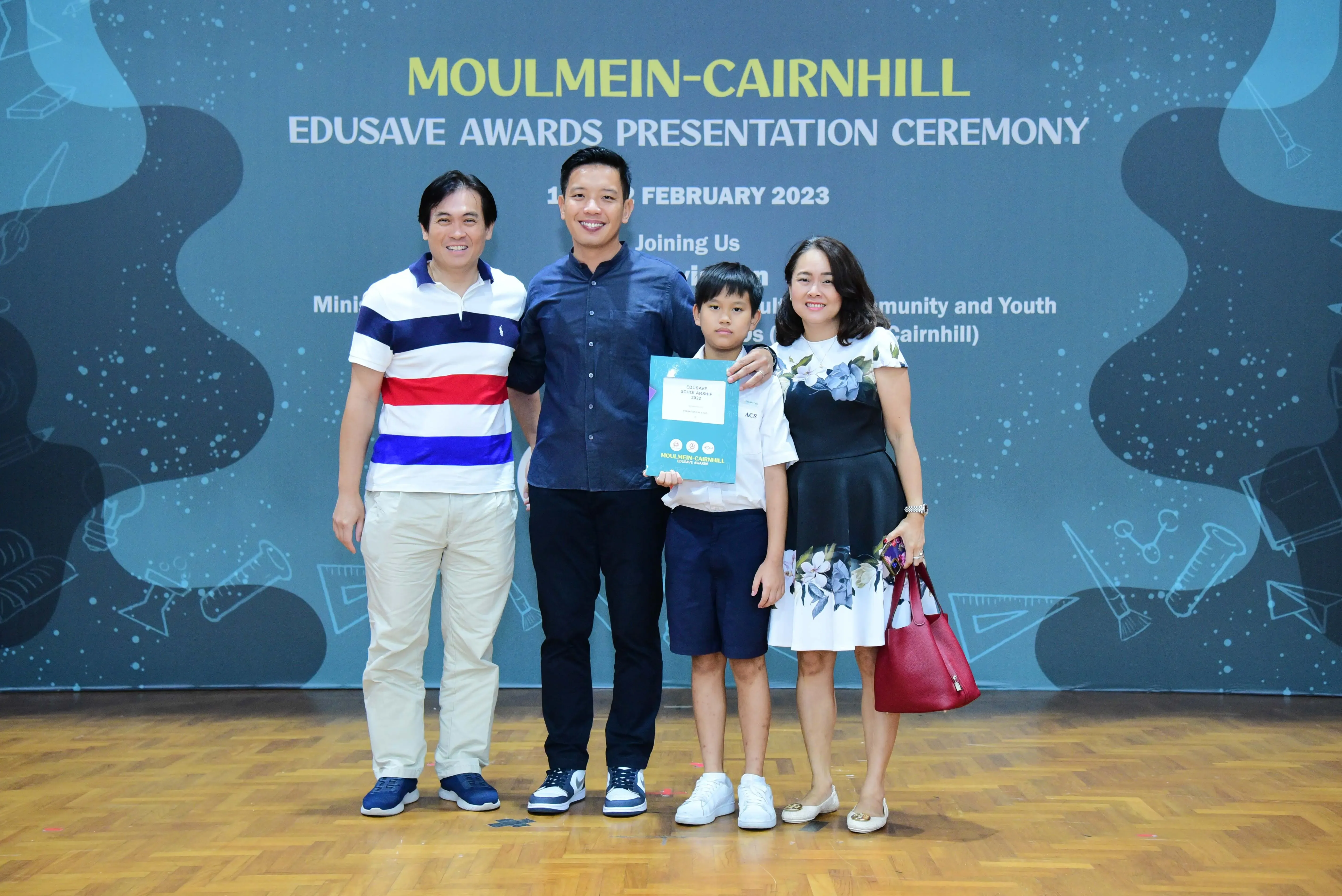 Three adults and a boy holding a certificate pose at the Moulmein-Cairnhill Edusave Awards Ceremony, February 2023.