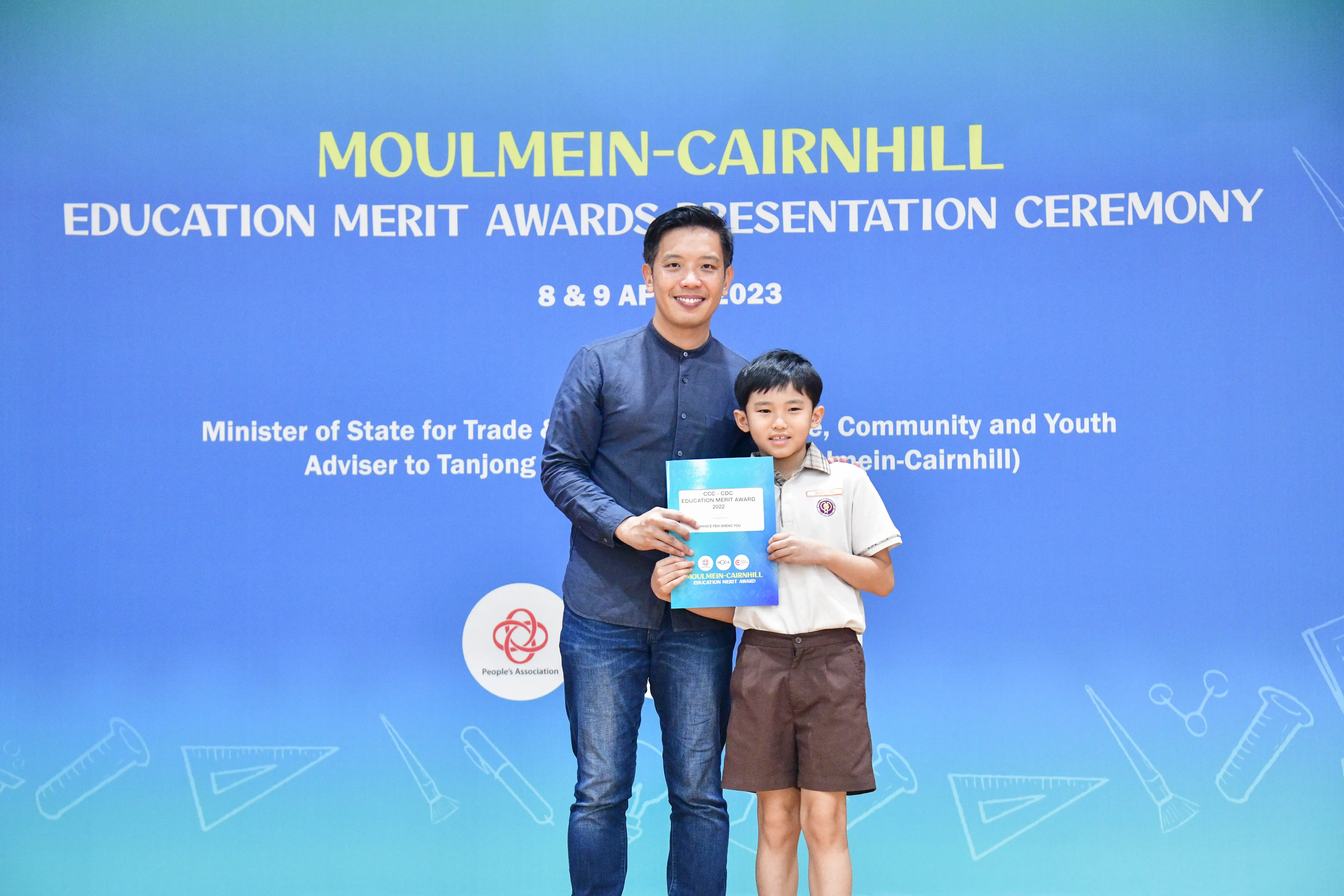 A man and a young boy in school uniform hold a certificate at the Moulmein-Cairnhill Education Merit Awards 2023.