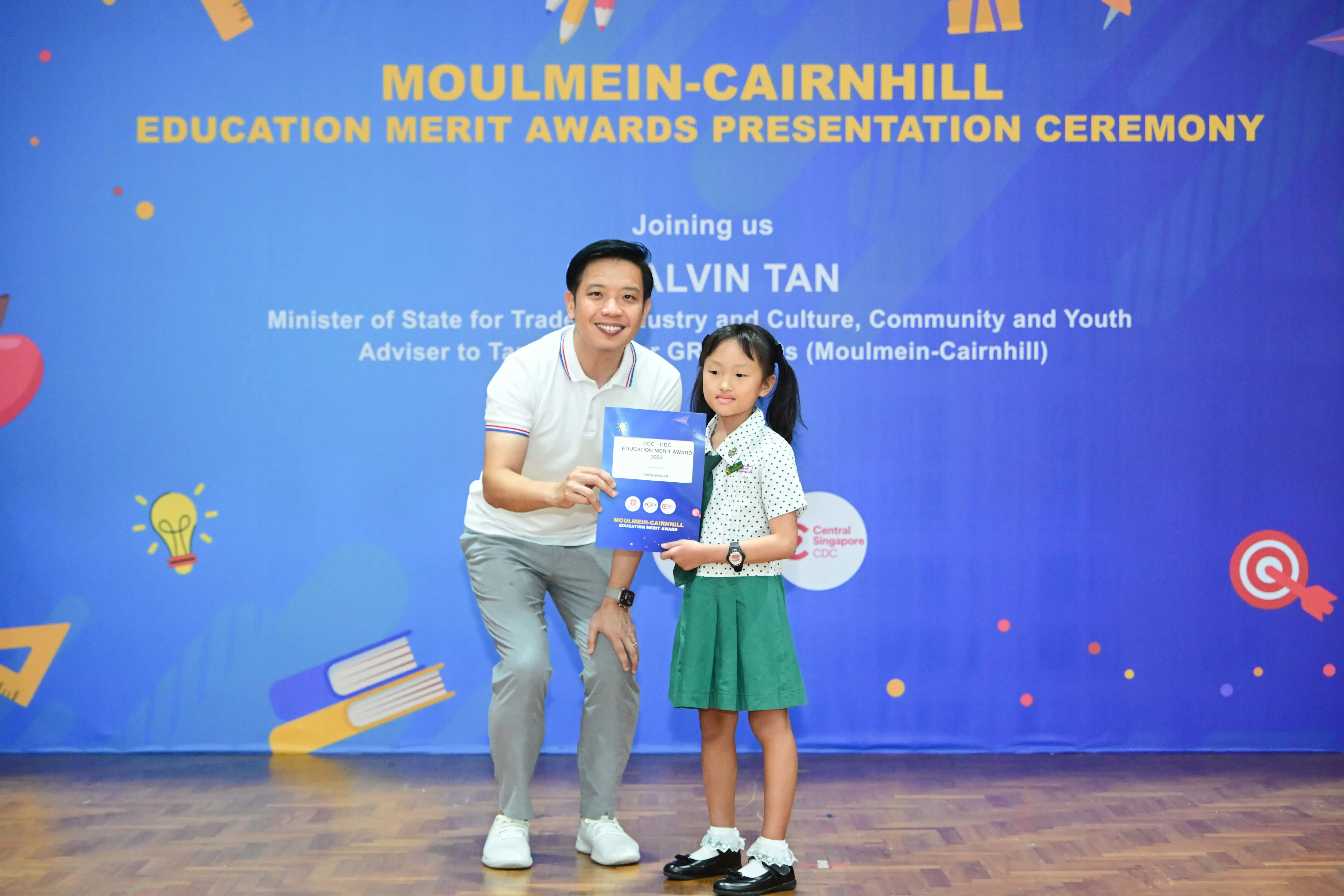 A man and a young girl hold a certificate at the Moulmein-Cairnhill Education Merit Awards Presentation Ceremony.