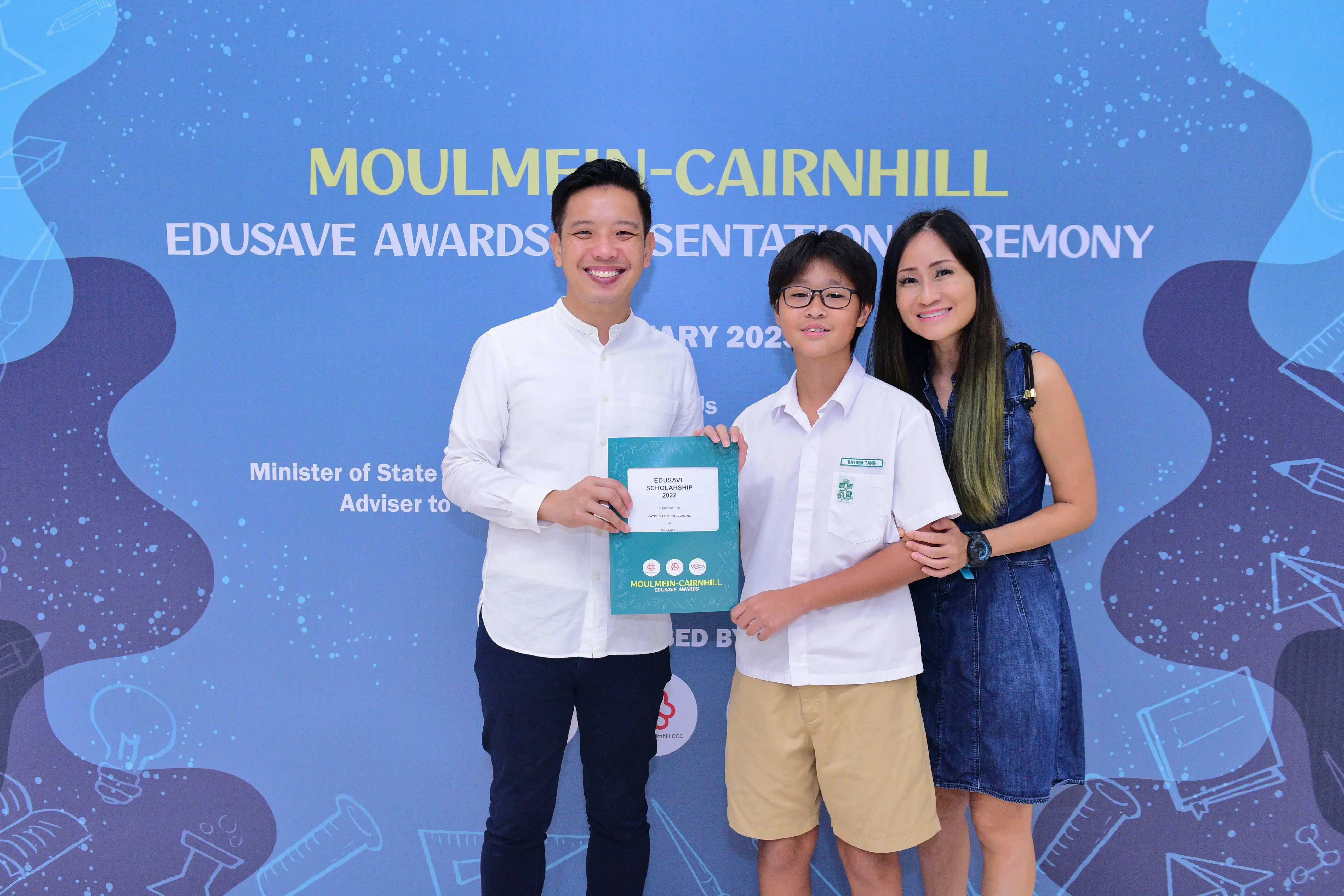 Three people pose with an Edusave Scholarship 2022 certificate at the Moulmein-Cairnhill Edusave Awards Ceremony.