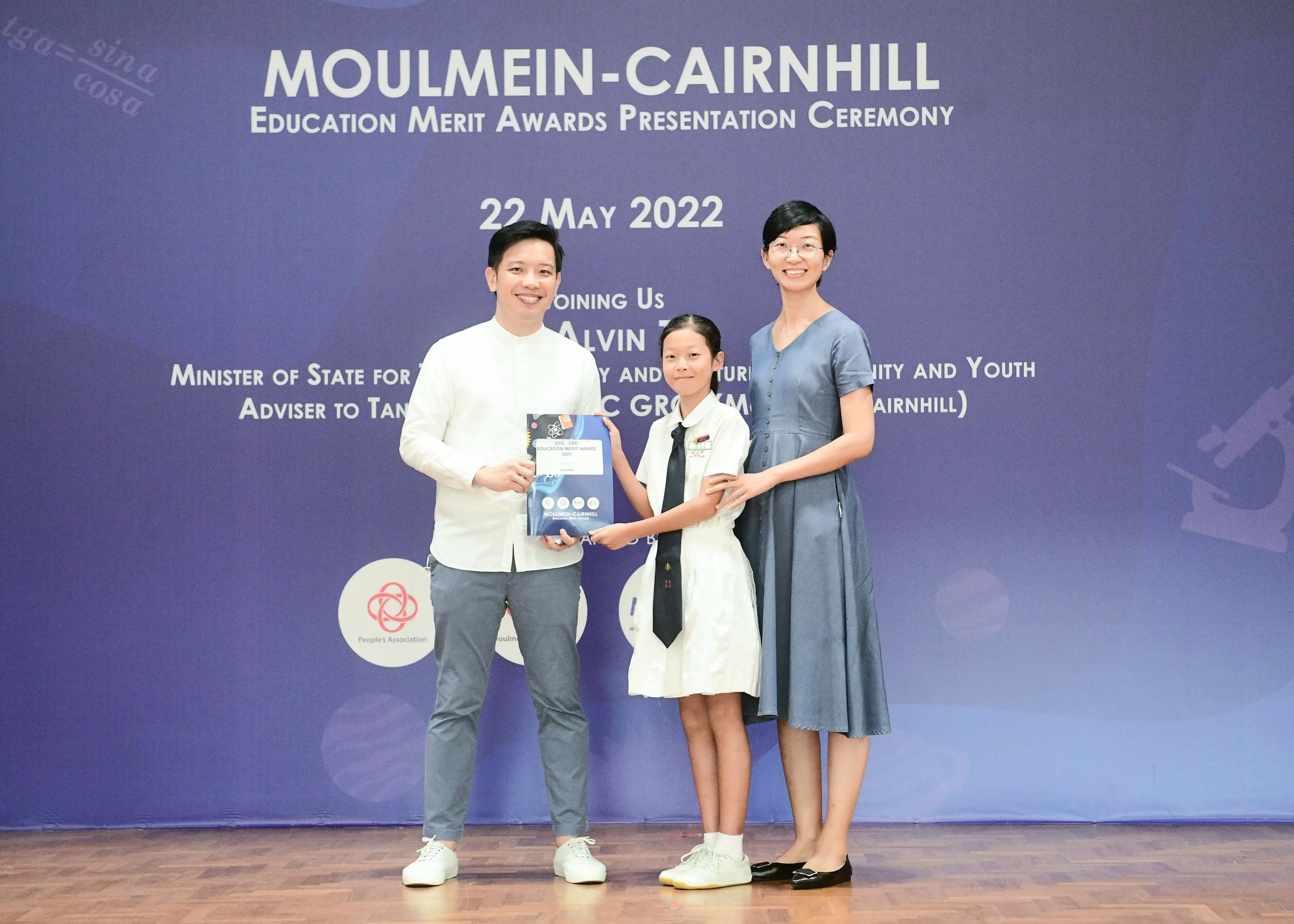 Two adults and a uniformed student pose holding an award at the Moulmein-Cairnhill Education Merit Awards on 22 May 2022.