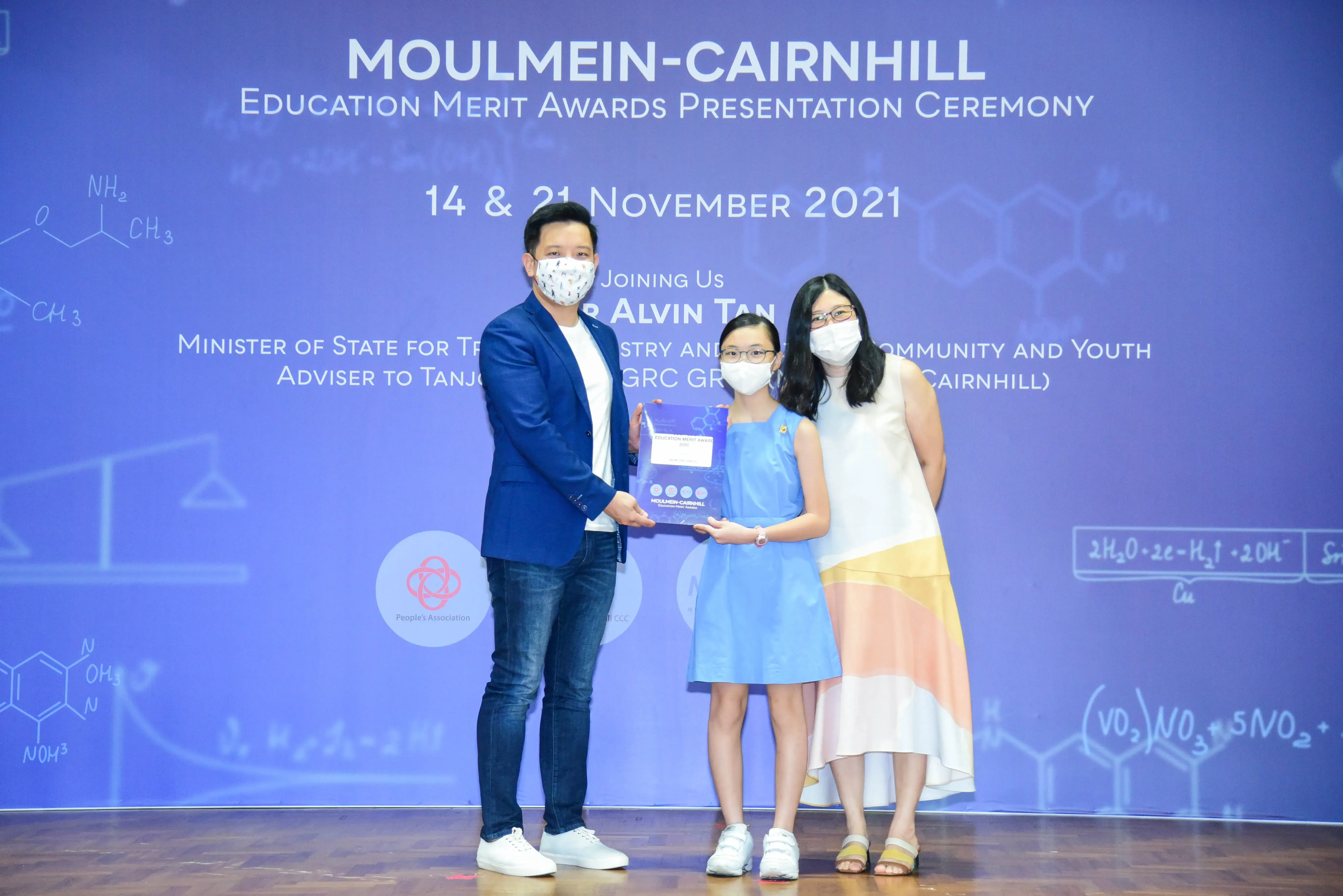 Three masked people pose on stage at the Moulmein-Cairnhill Education Merit Awards Ceremony, November 2021.