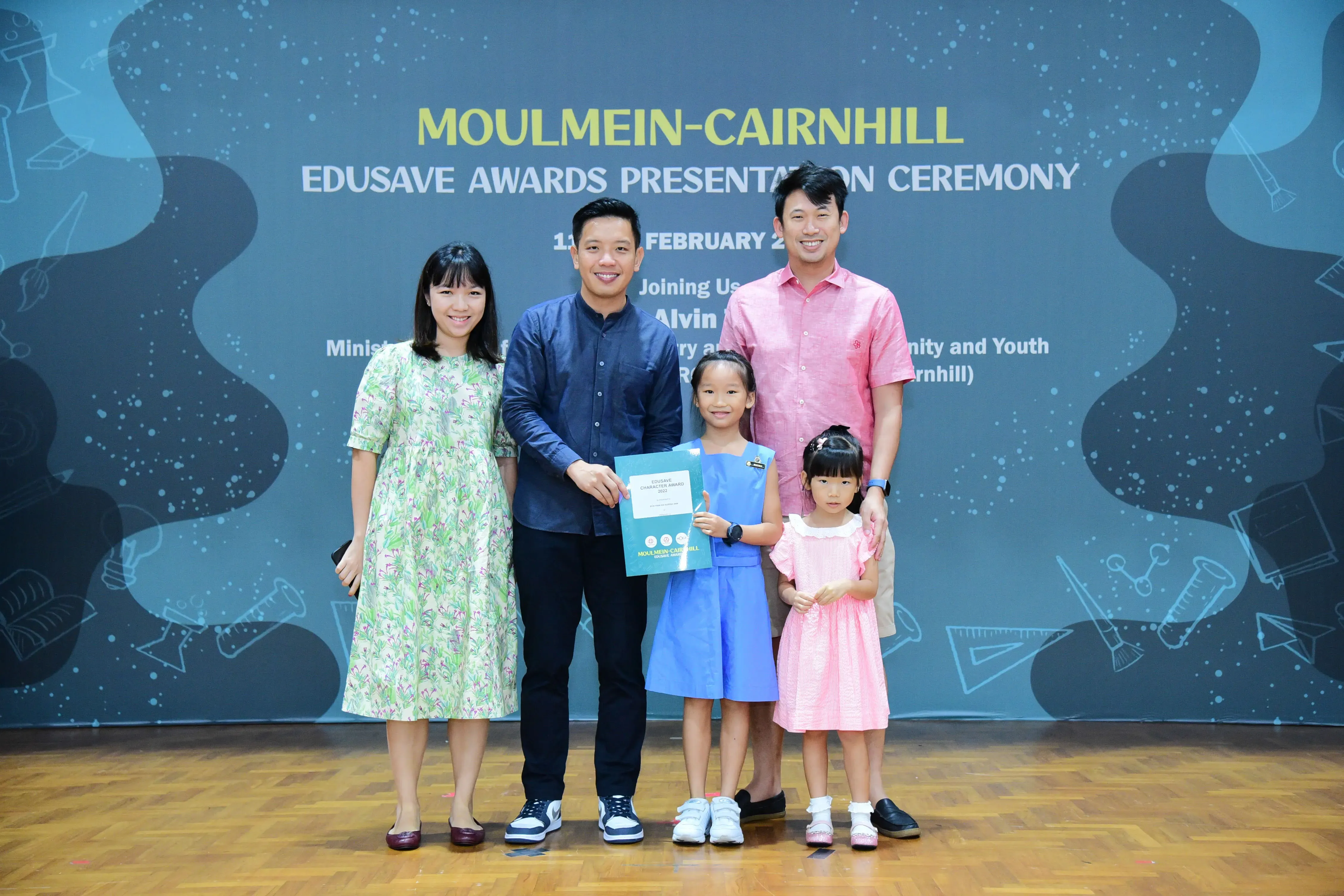 Two adults and two young girls pose at the Moulmein-Cairnhill Edusave Awards Presentation Ceremony, holding a certificate.