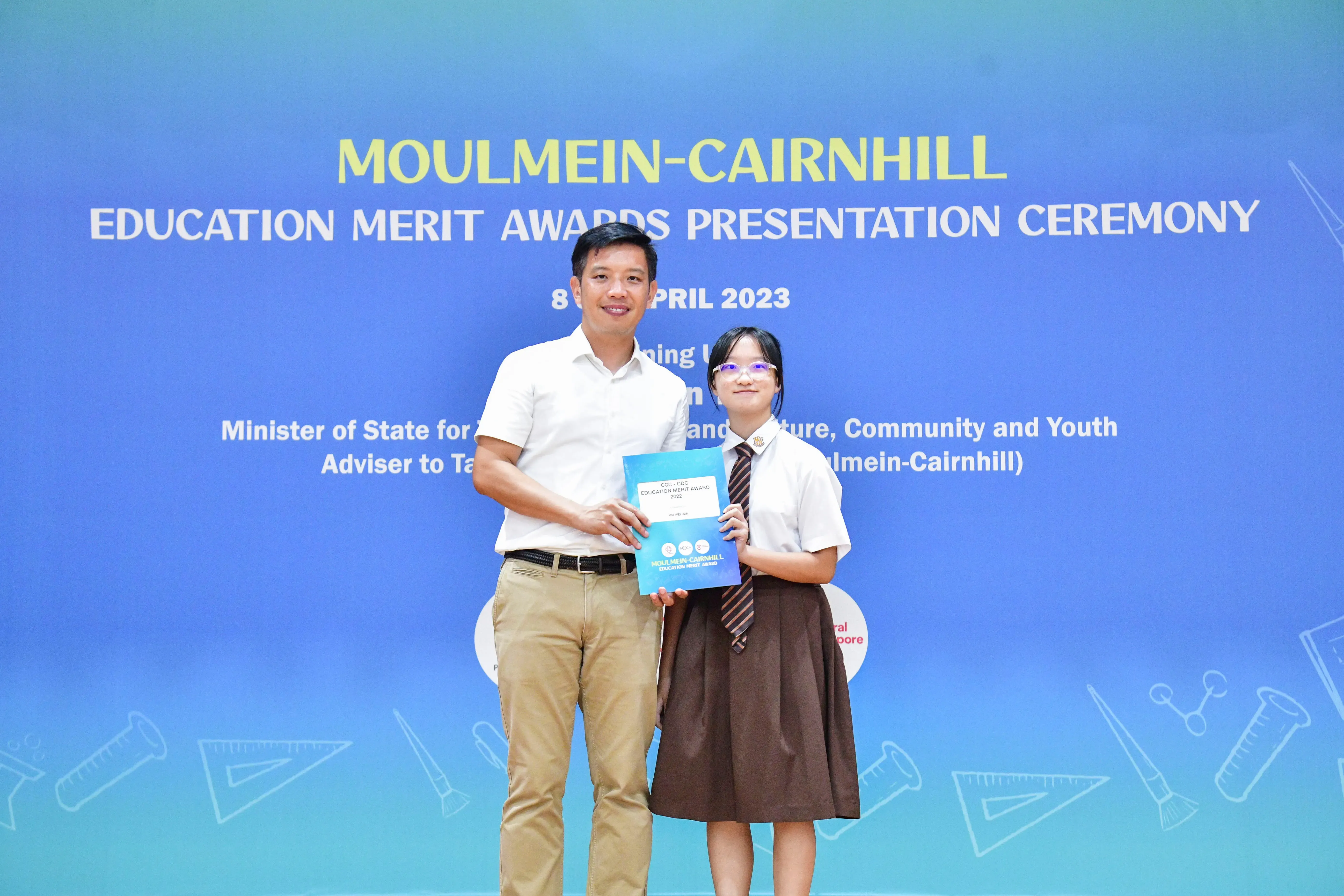 A man and a young girl in school uniform hold an award certificate at the Moulmein-Cairnhill Education Merit Awards 2023.