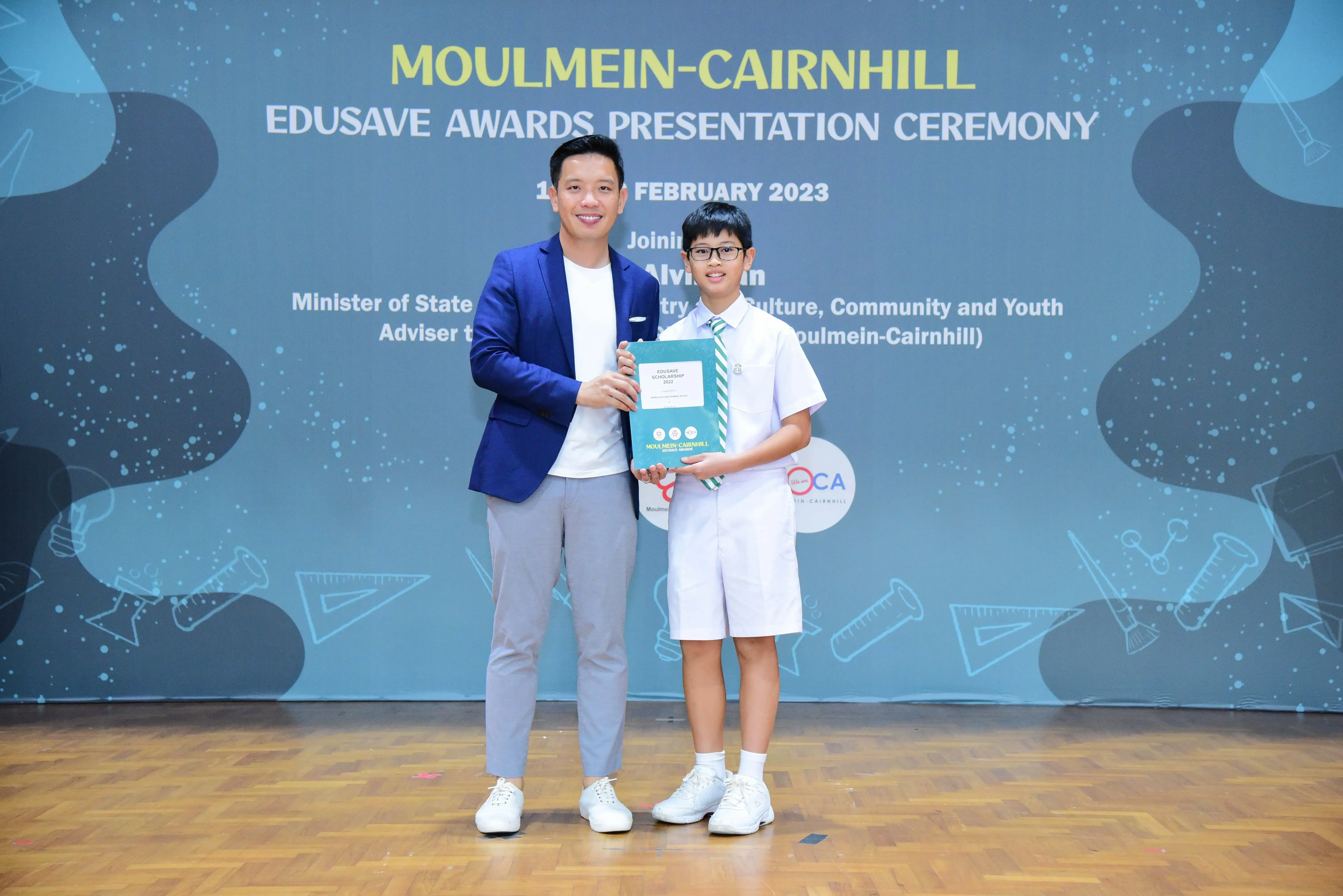 A man in a blue blazer and a young student in school uniform hold a certificate at the Moulmein-Cairnhill Edusave Awards 2023.